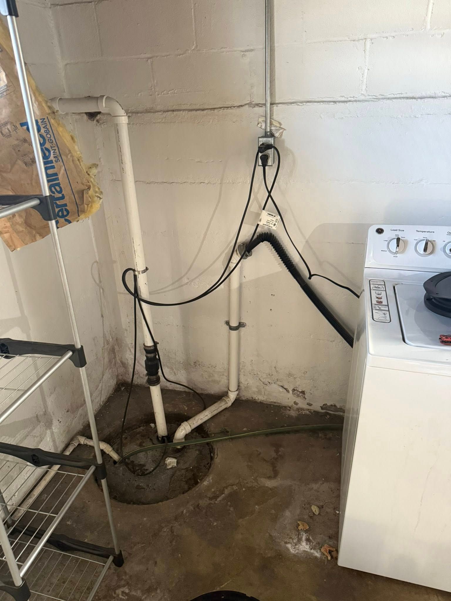 A sump pump installation with white PVC piping, a check valve, and electrical cords plugged into a wall outlet.