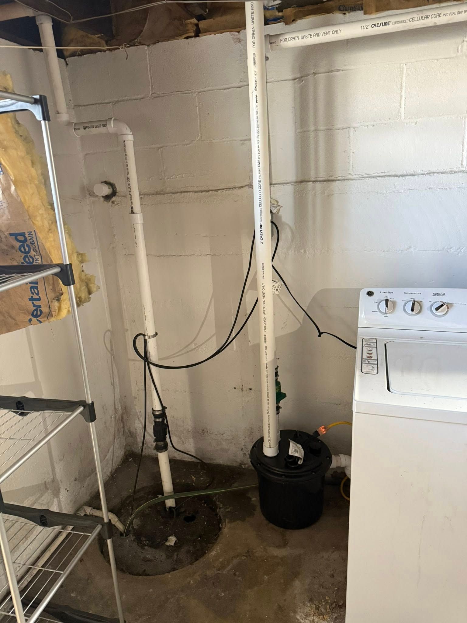 A basement corner featuring a sump pump and a sewage ejector pump system next to a white washing machine.