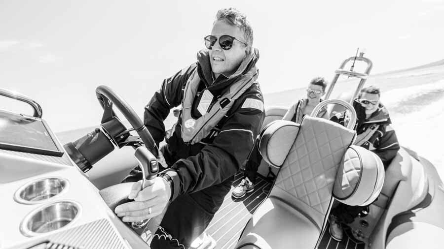 A man in a life jacket is driving a boat.