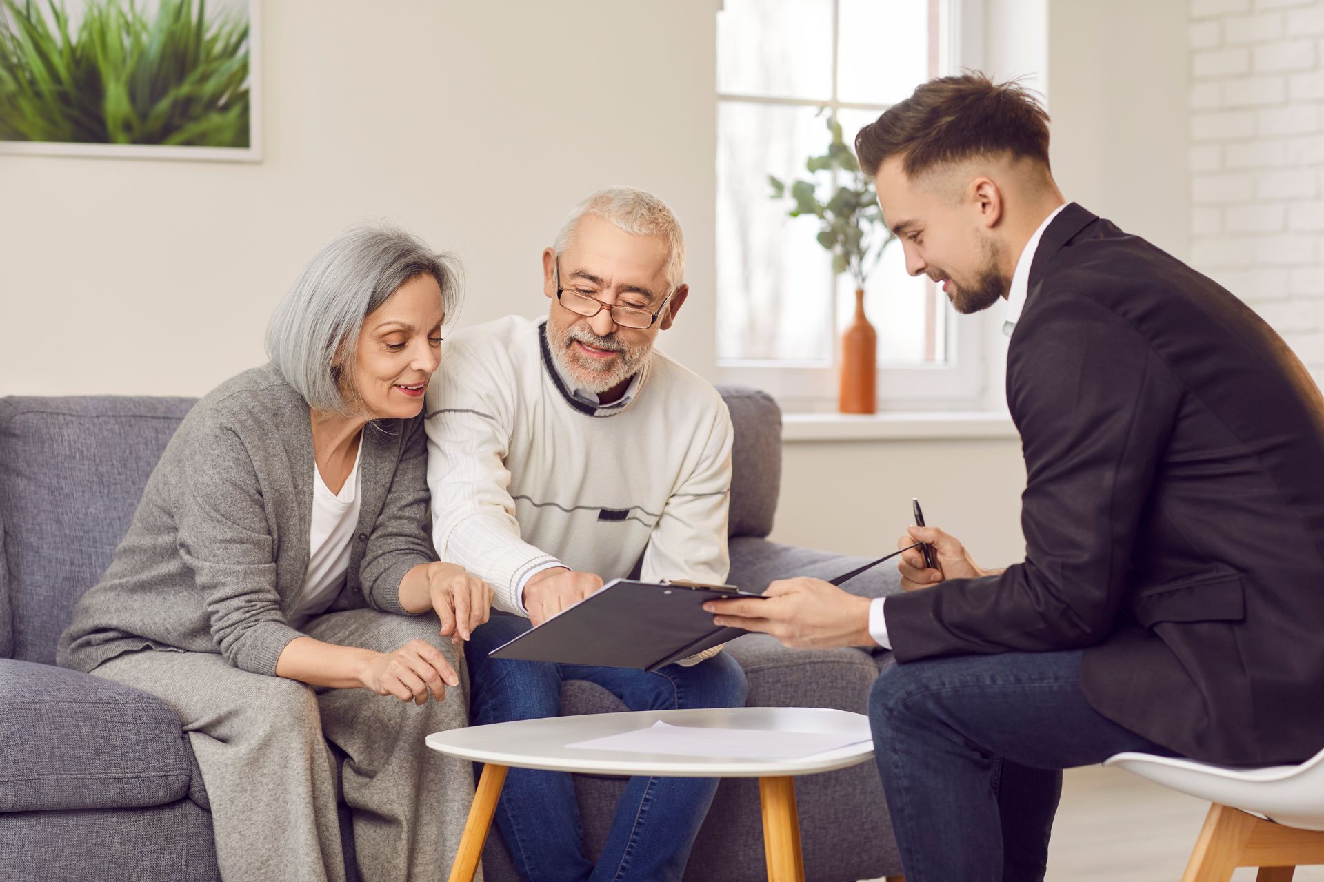 Elderly couple reviews retirement plans with advisor in cozy living room.