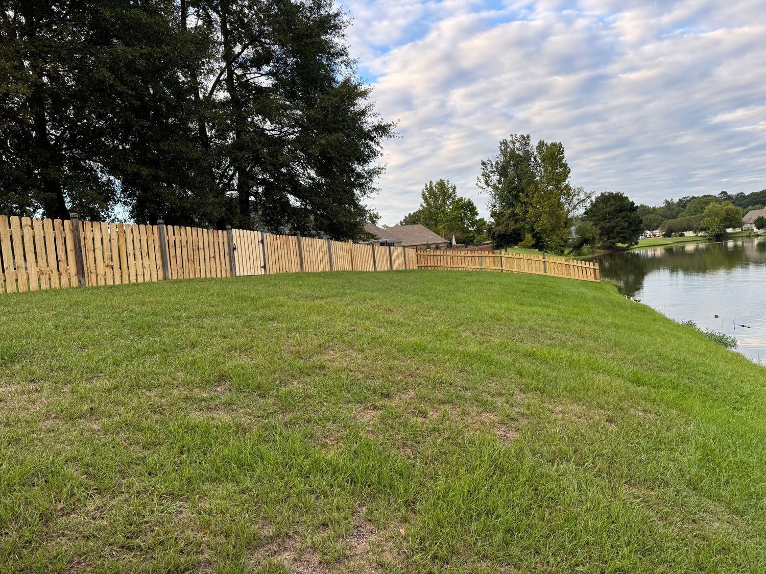 A wooden fence surrounds a grassy field next to a lake.