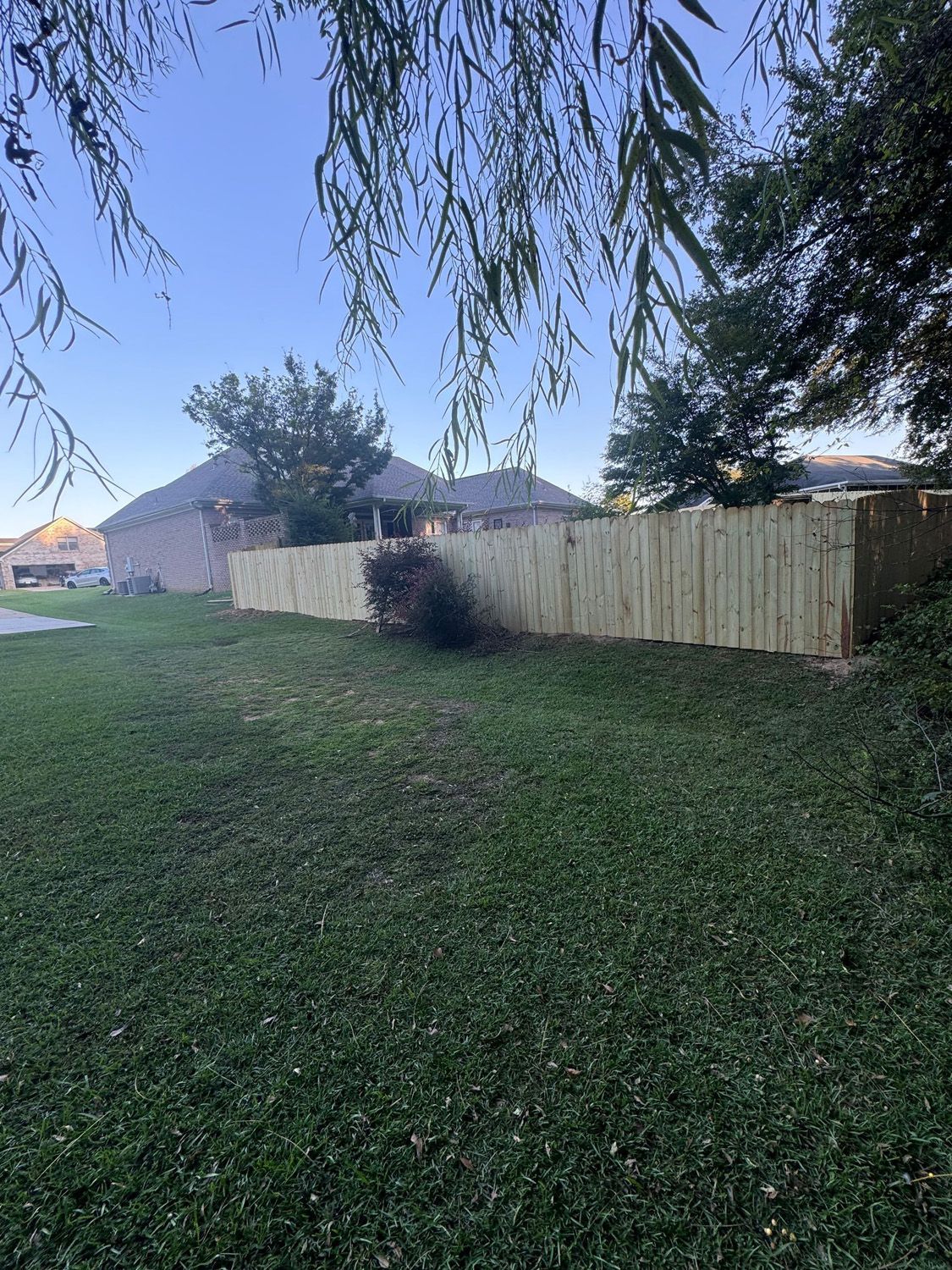 A wooden fence is in the middle of a lush green yard.