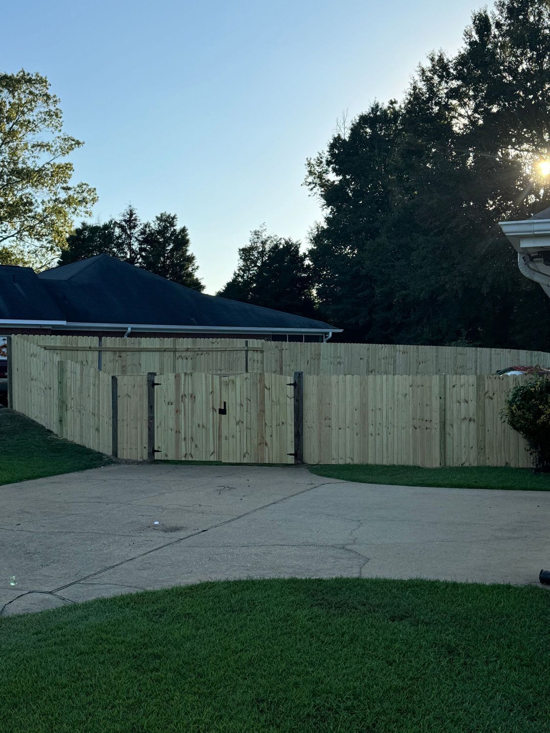 A wooden fence surrounds a driveway in front of a house.