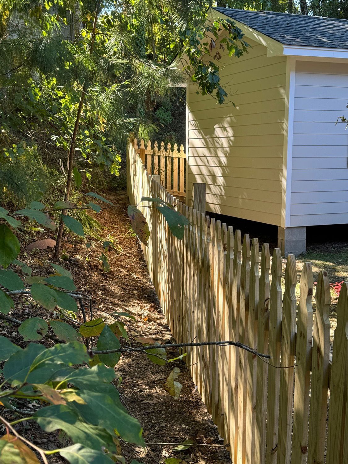 A wooden fence surrounds a yellow shed in the woods.