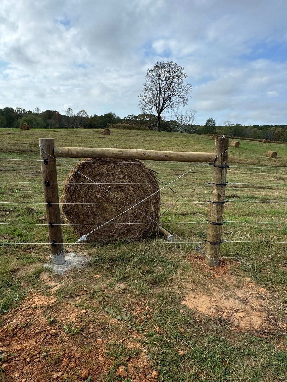 A bale of hay is behind a barbed wire fence in a field.