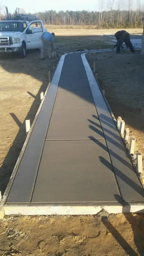 Newly poured concrete driveway leading to a house with a person in a yellow shirt walking on the grass.