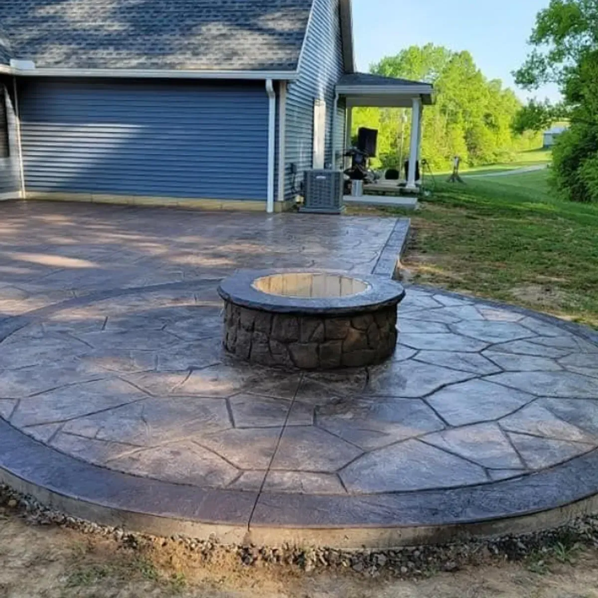 Circular stone patio with fire pit, leading to a home with a garage, and a small porch.
