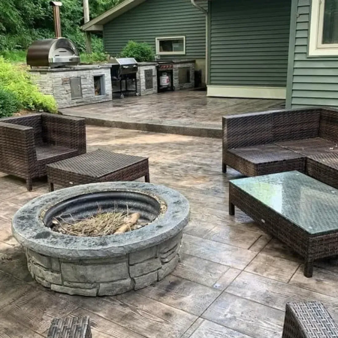 Outdoor patio with fire pit and seating near a green house and outdoor kitchen.