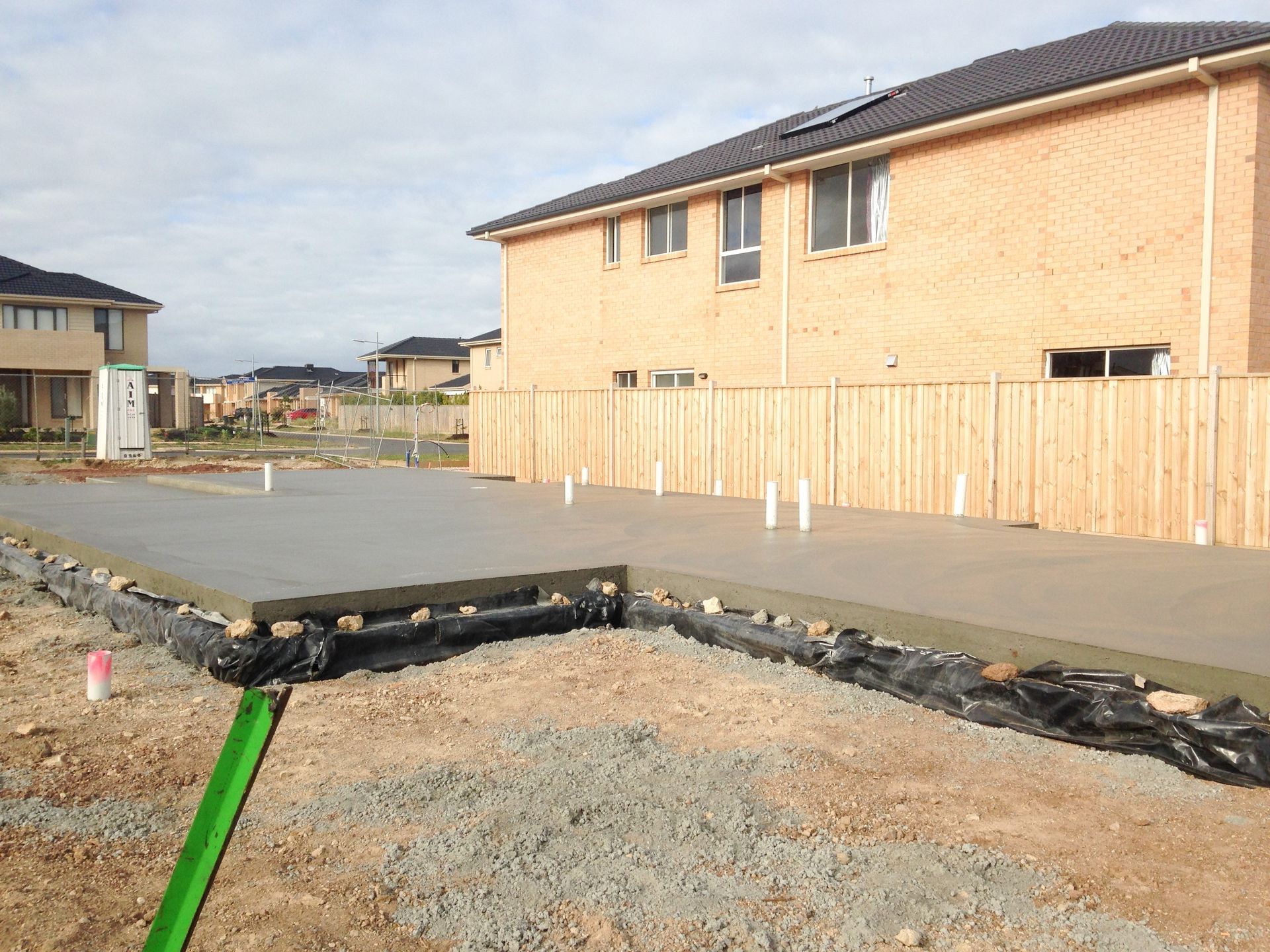 A new concrete foundation for a house, next to a wooden fence and a two-story brick building.