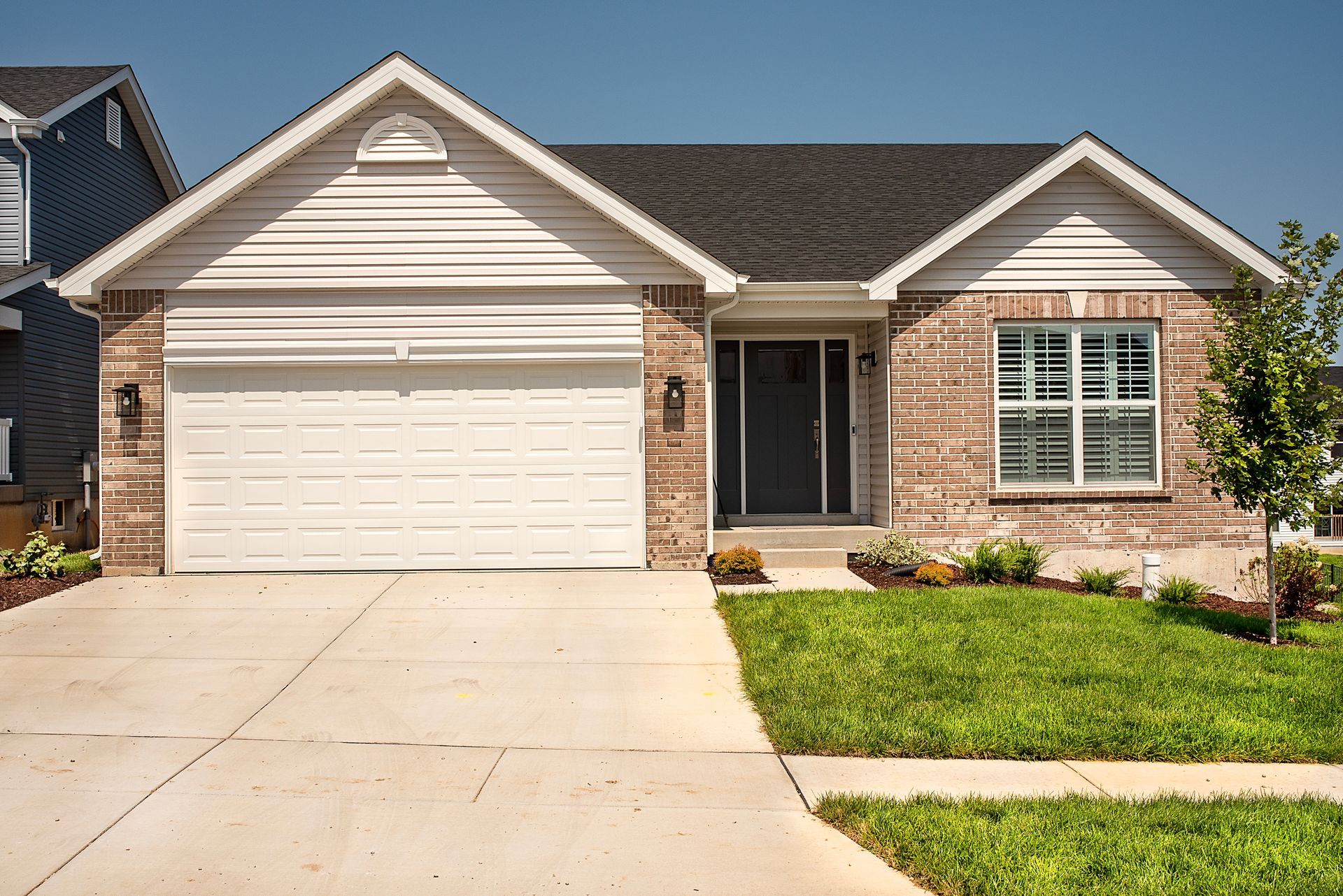 Single-story brick home with a garage, front lawn, and a blue sky.