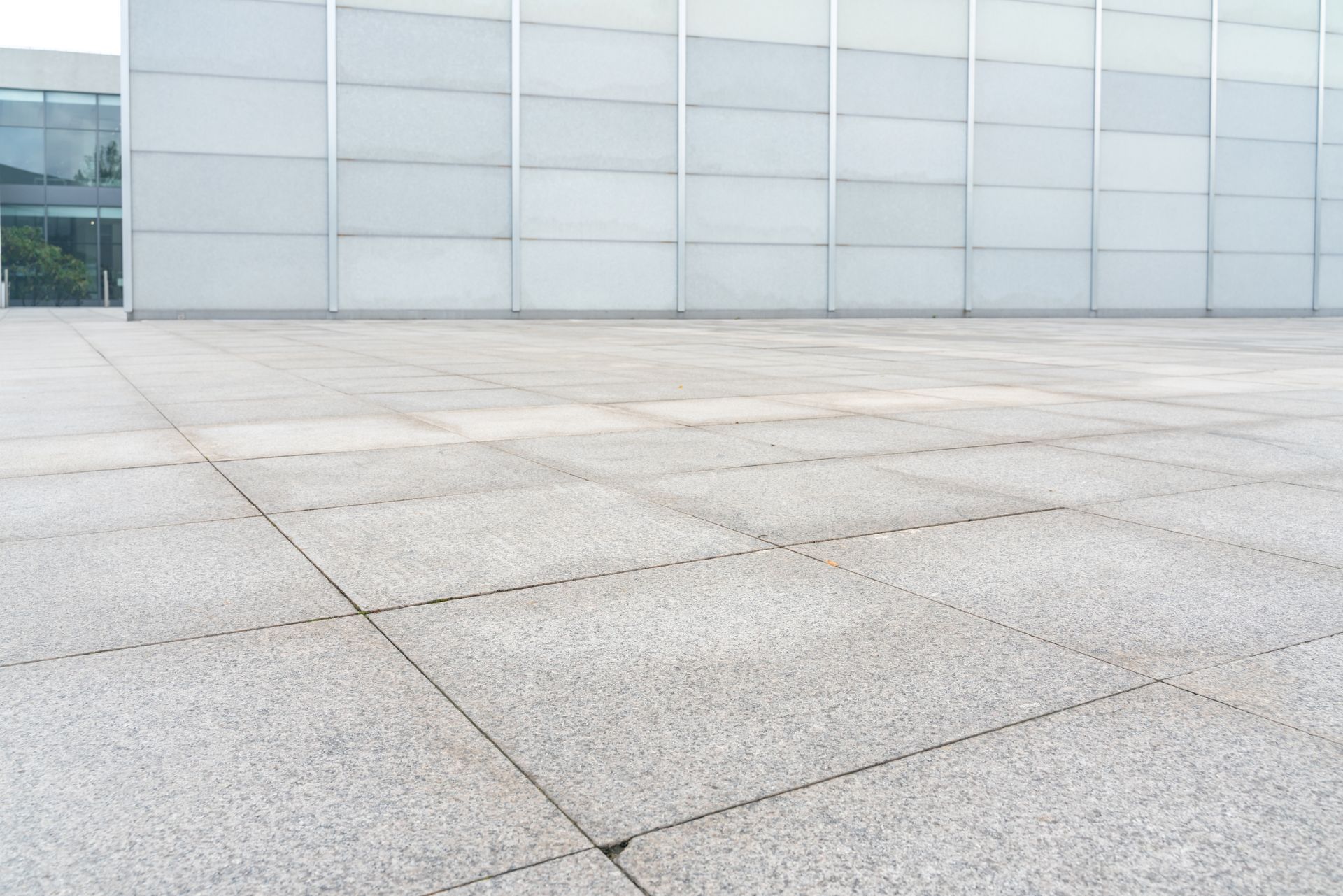 Light gray tiled plaza in front of a modern, white building with glass windows.