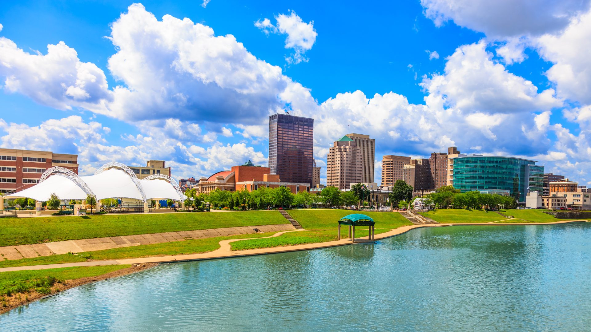 A city skyline with a lake in the foreground and a park in the background.