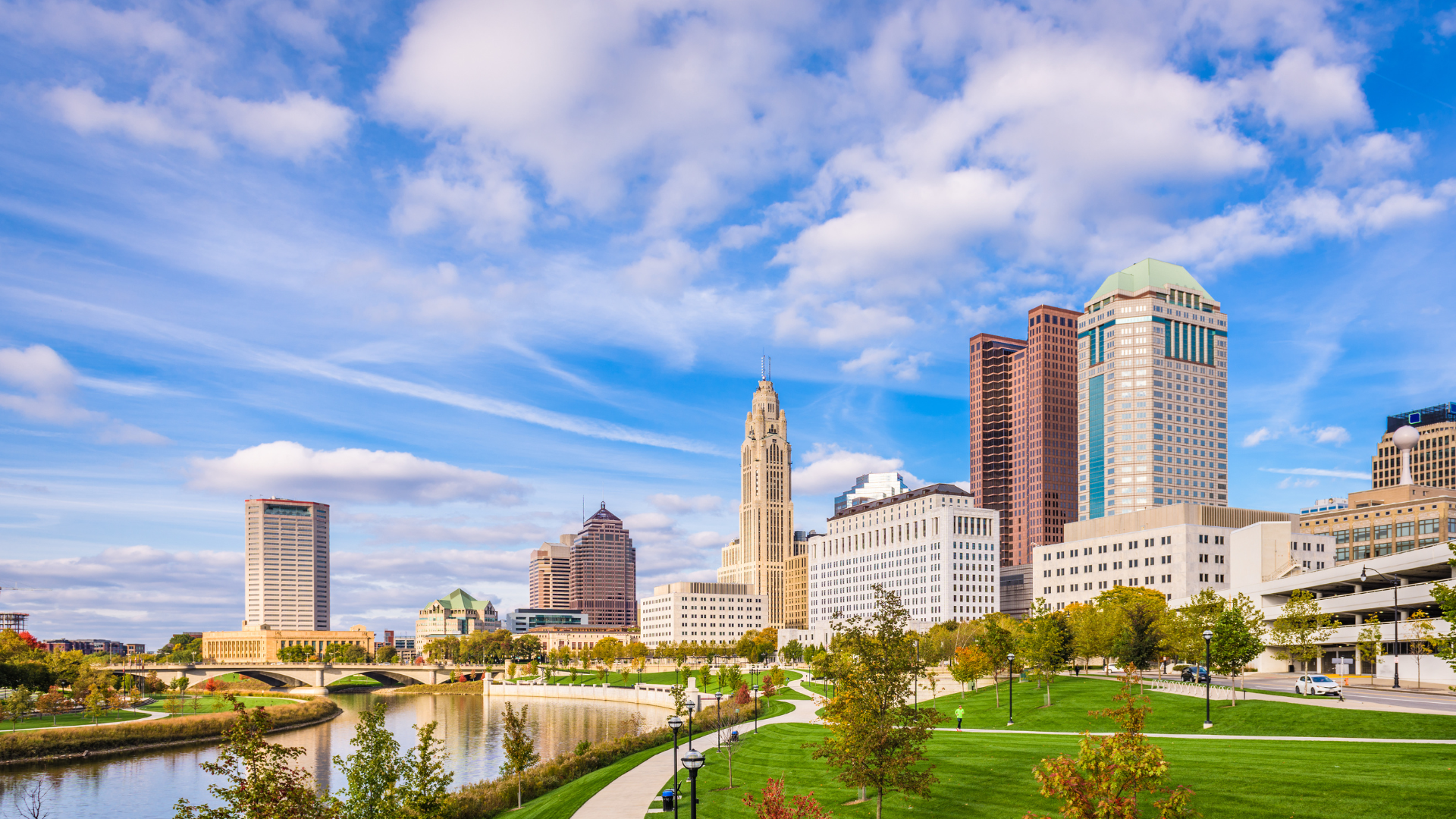 A city skyline with a river in the foreground and a park in the background.