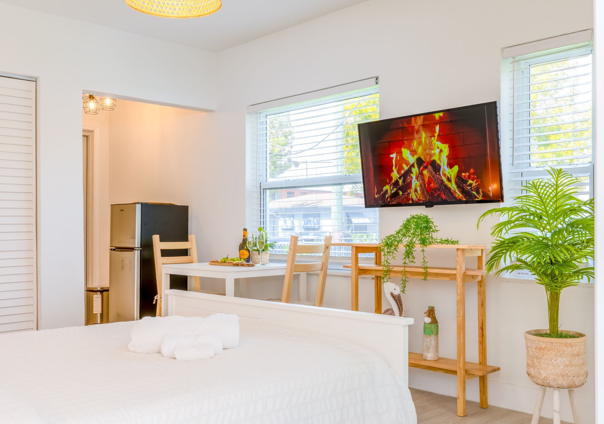Cozy studio apartment with bed, TV, dining area, and plants near a window.