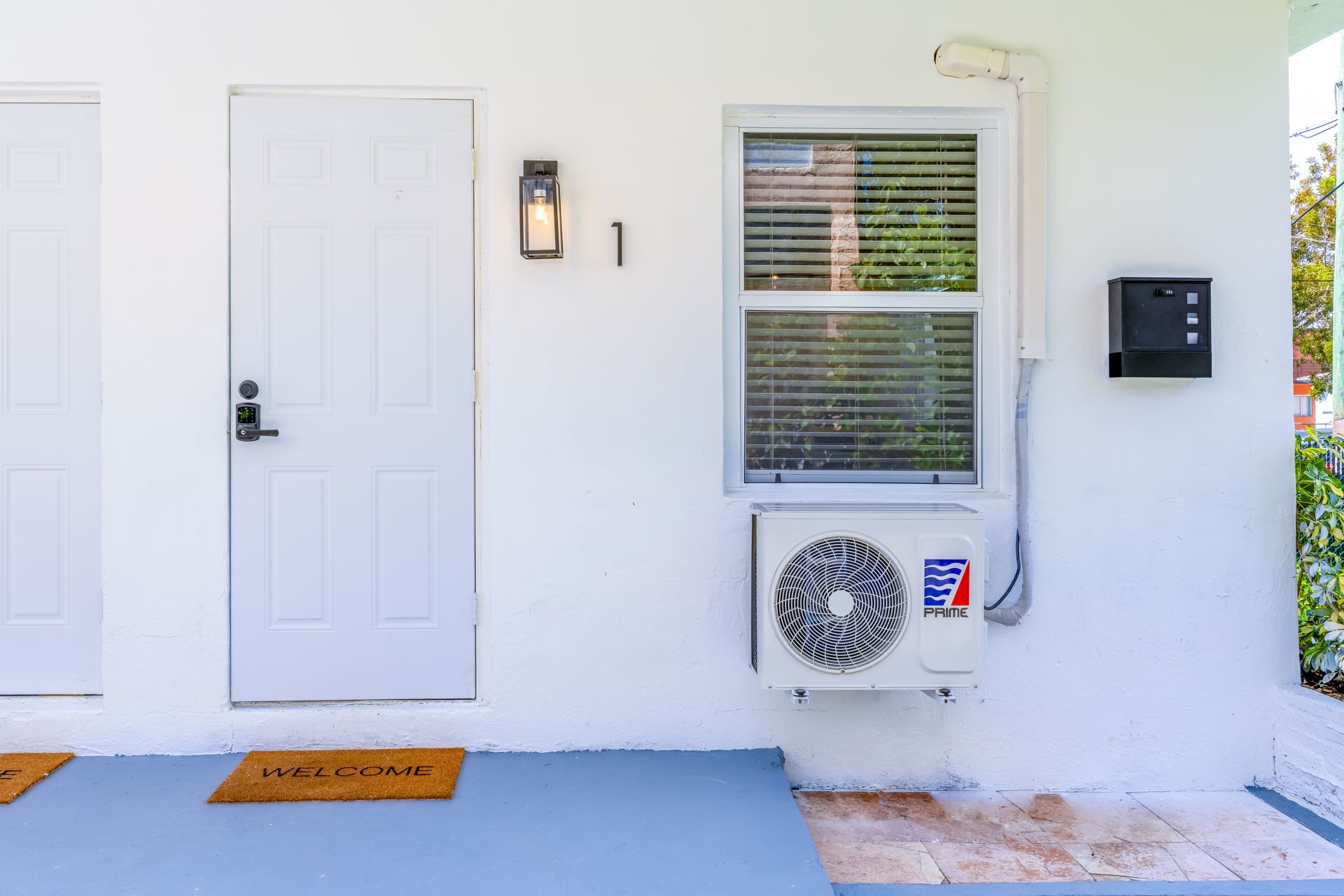 White building exterior with door, window, AC unit, and welcome mat.