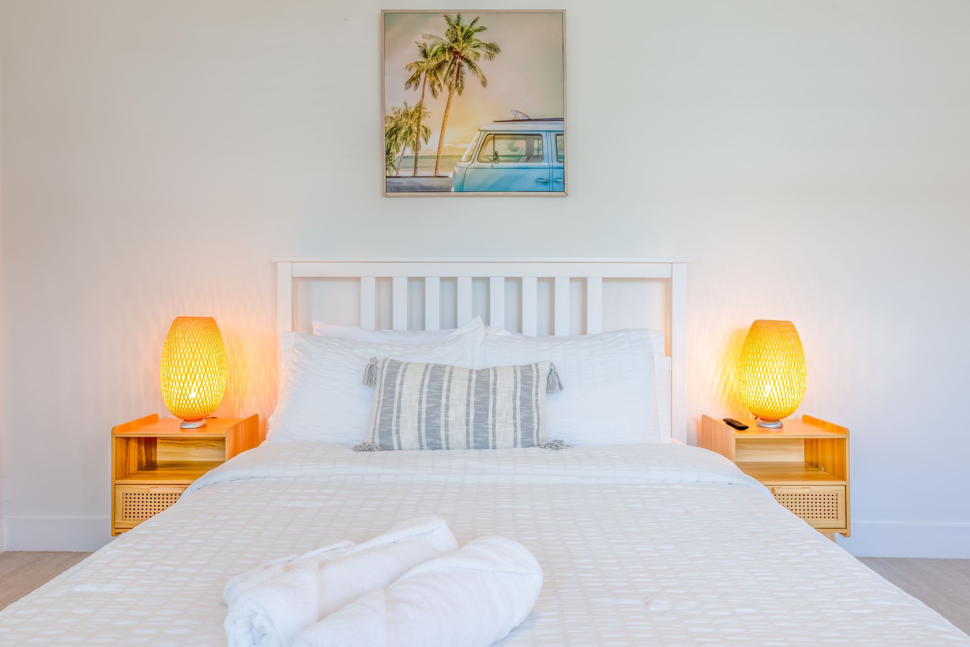 White bedroom with bed, nightstands, lamps, and beach artwork.