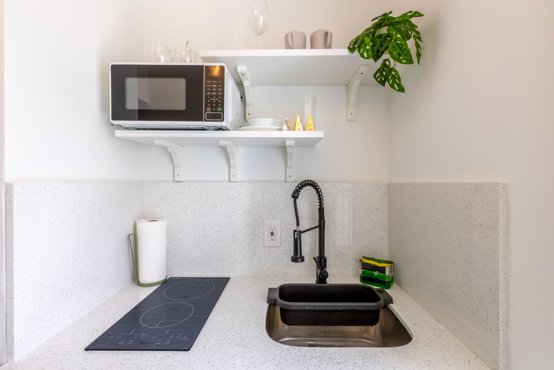 Small kitchen with a microwave, sink, and stovetop on a speckled white countertop.