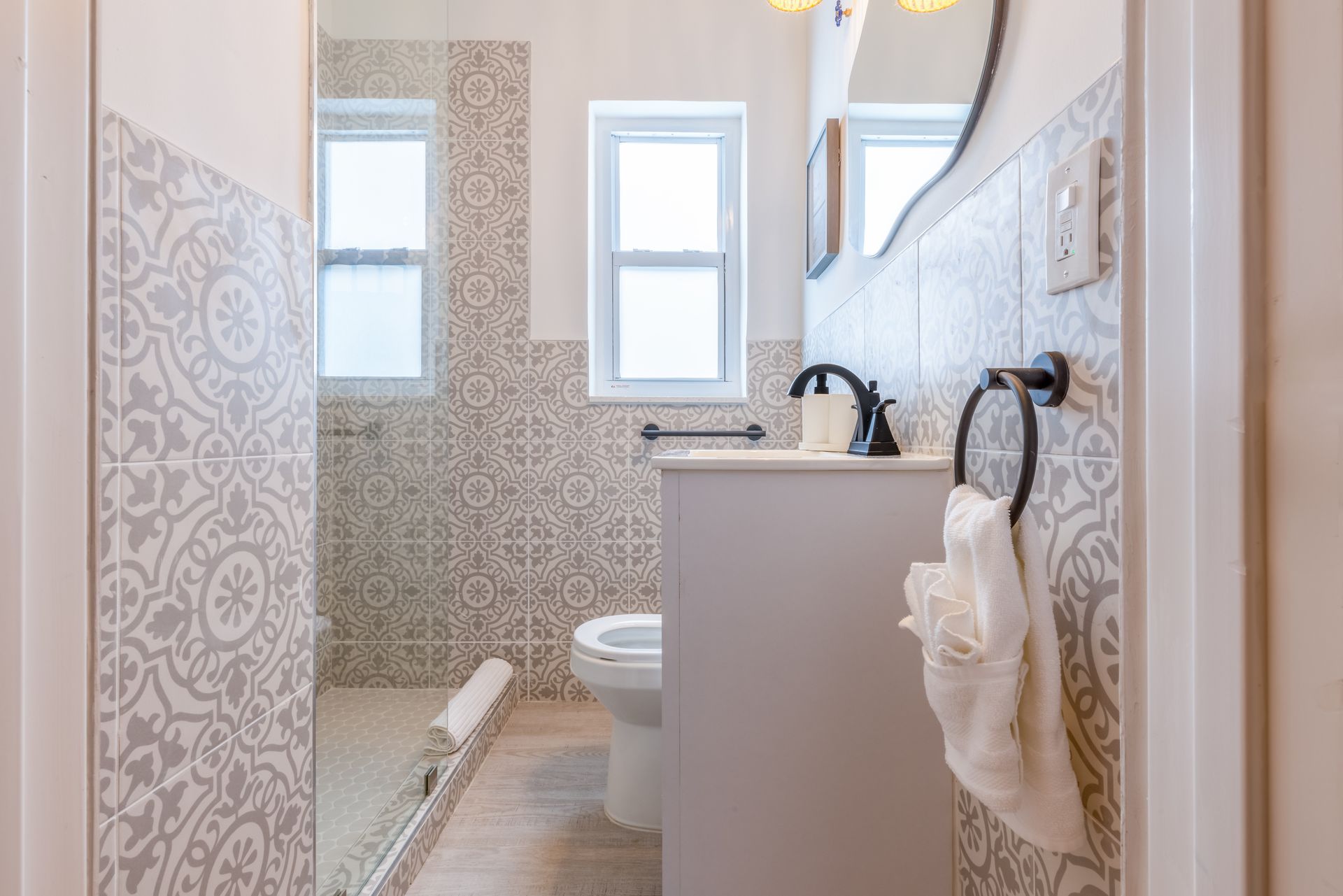 Small bathroom with patterned tile walls, a vanity, toilet, and towel rack.