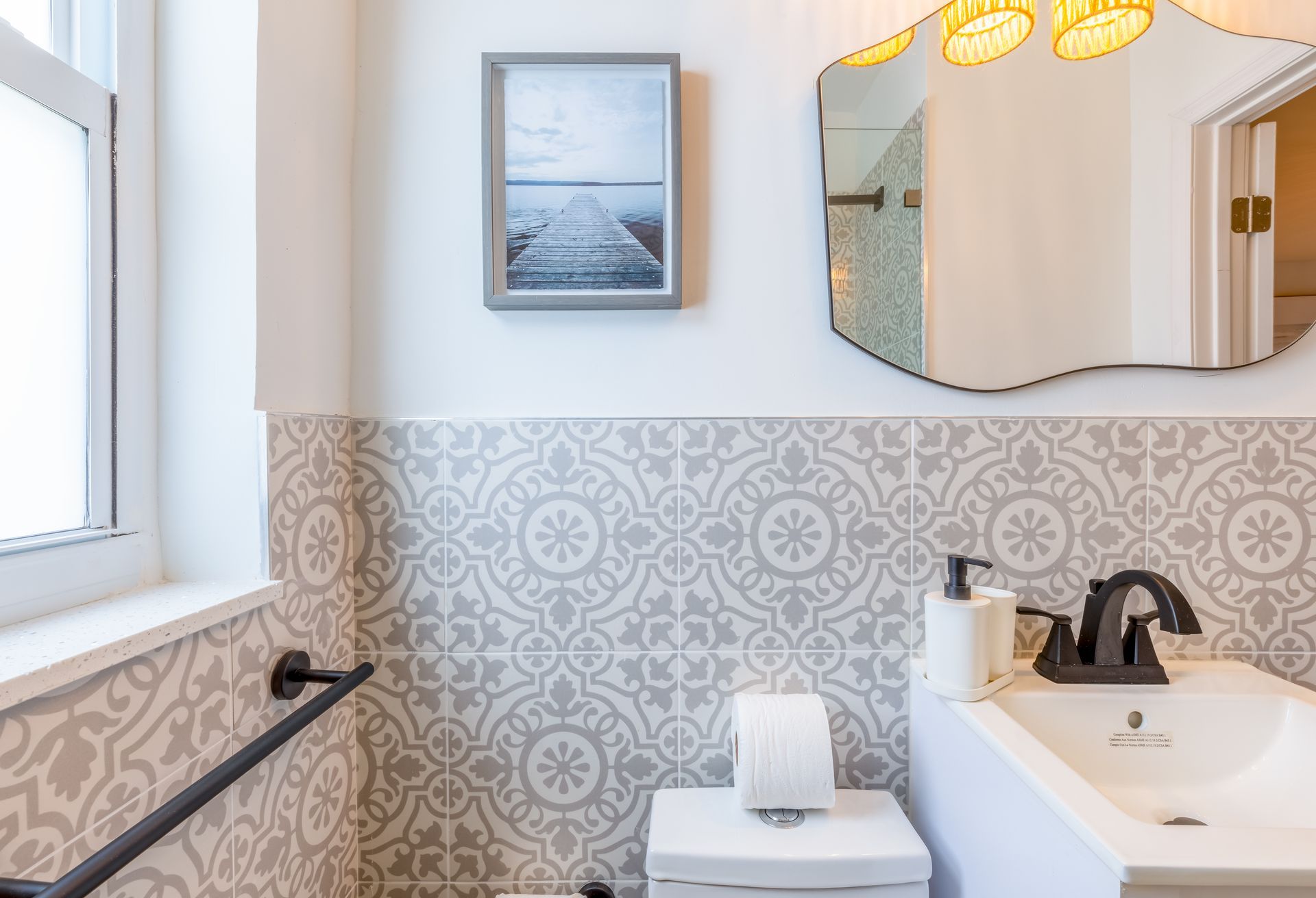 Bathroom with patterned gray and white tile, small sink, mirror, and art.