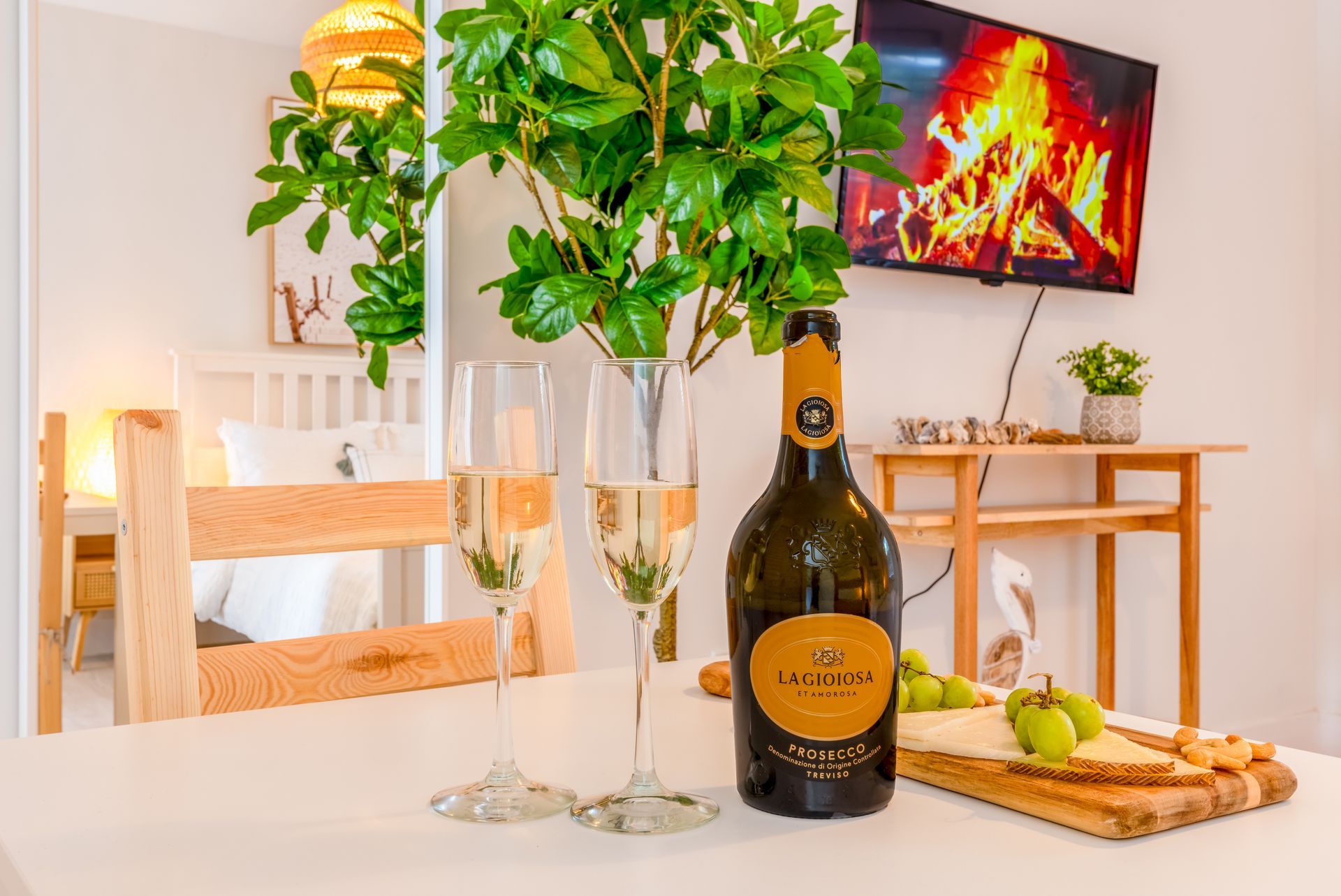Table set for a romantic evening: champagne, glasses, snacks, and a TV with a fireplace.