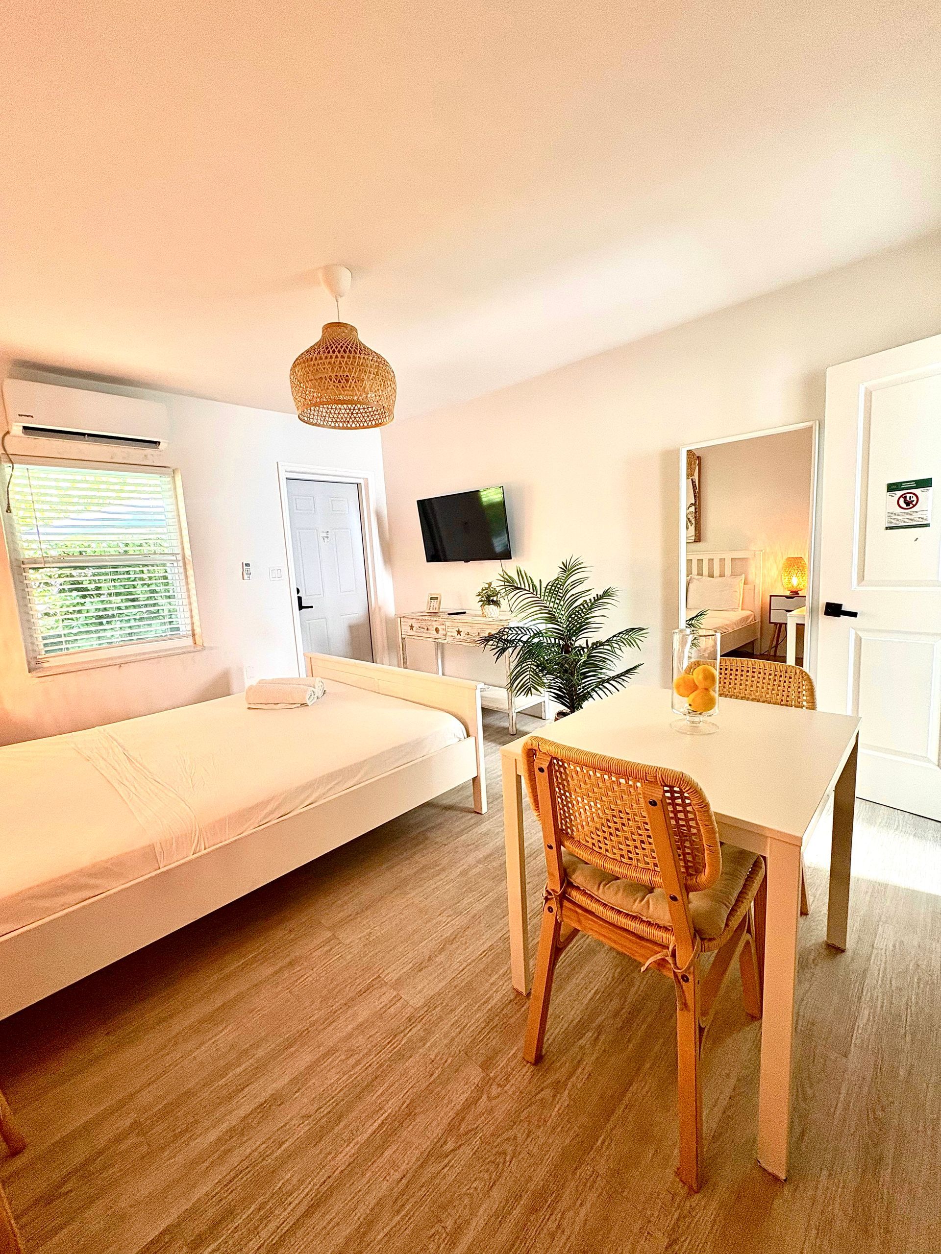 Bright studio apartment with white walls, a bed, table, and natural light.