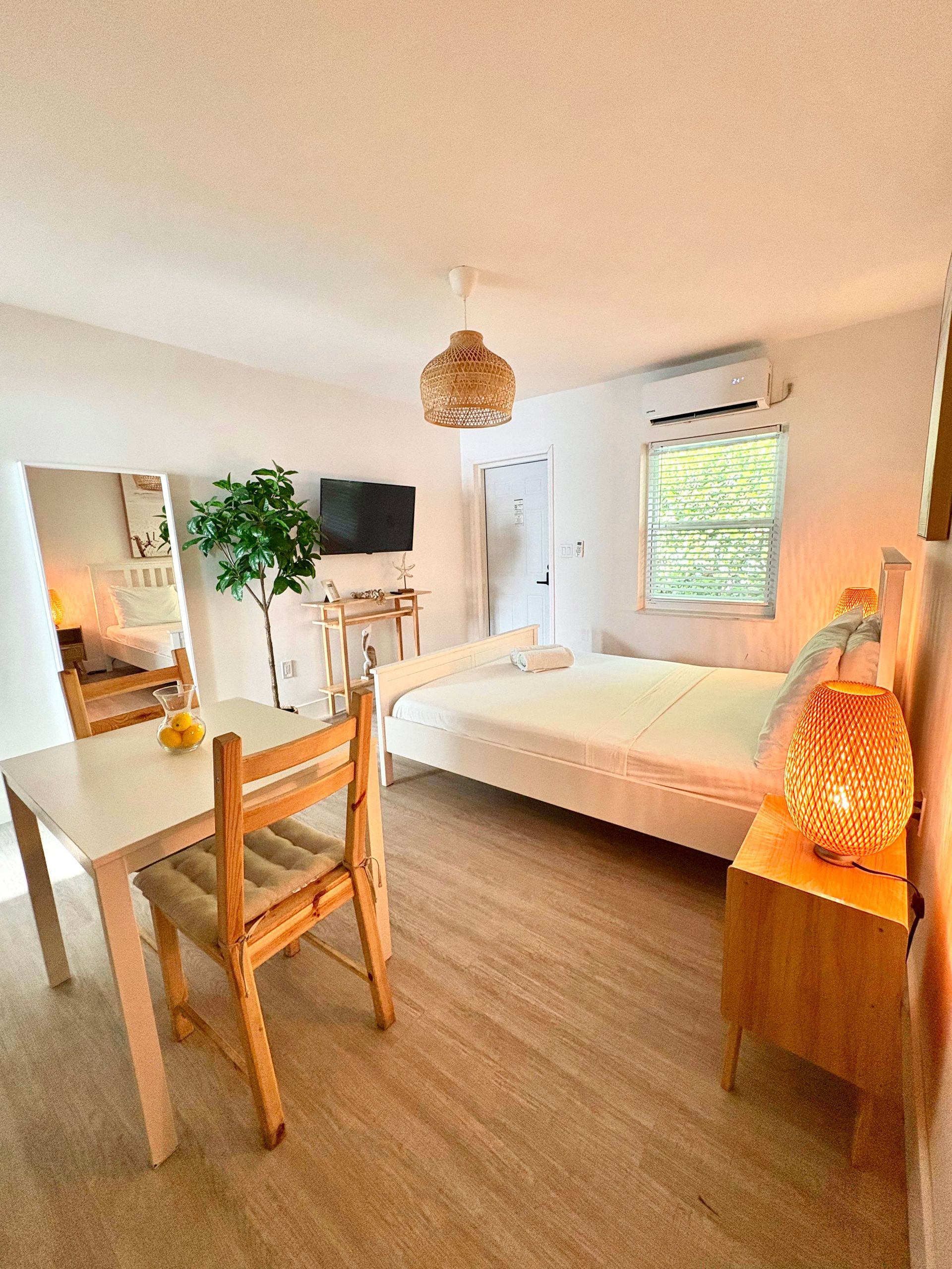 Cozy studio apartment with bed, desk, chair, and nightstand with a woven lamp.
