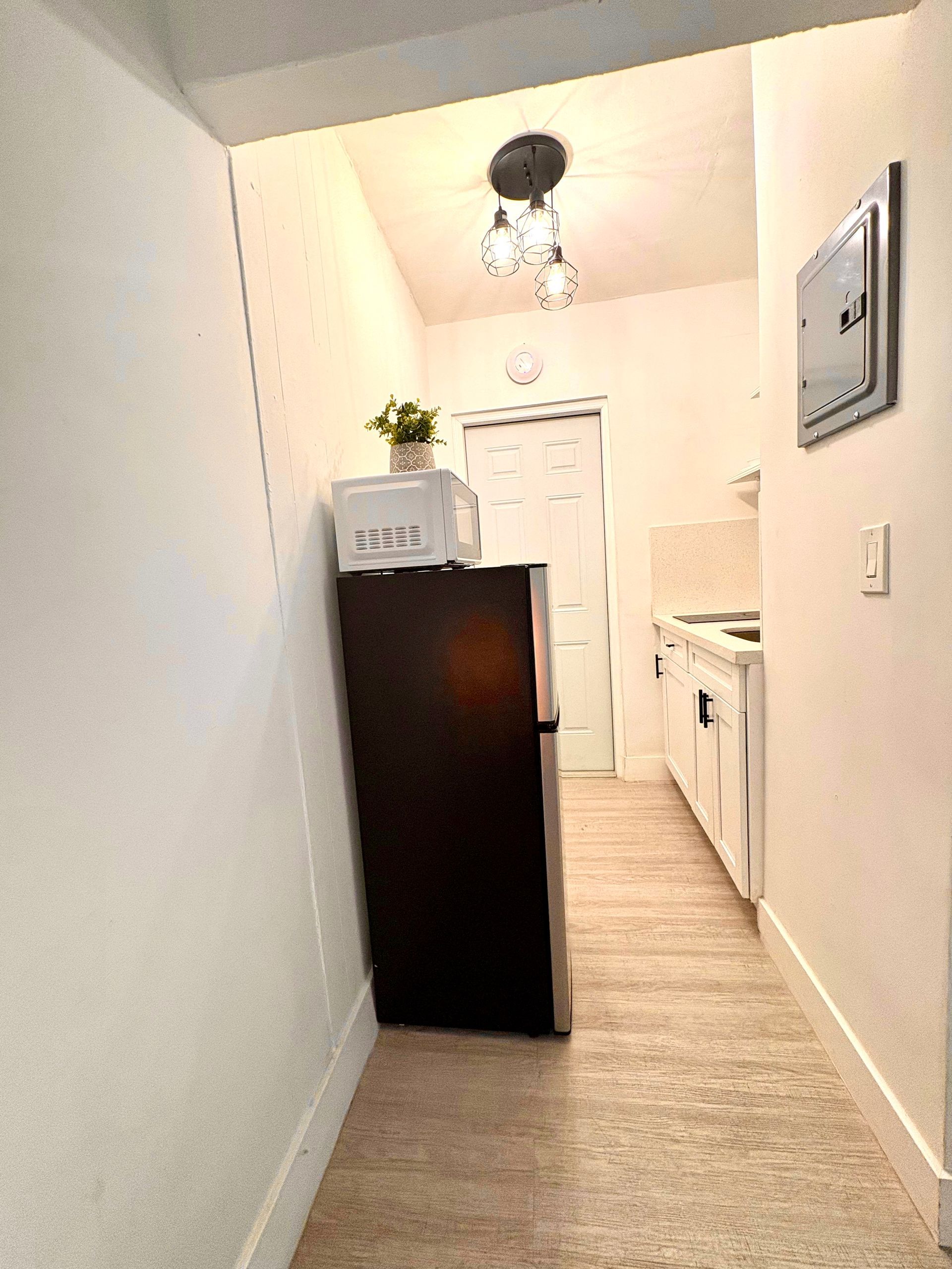 Narrow hallway with white walls, a dark refrigerator, and a small kitchen.