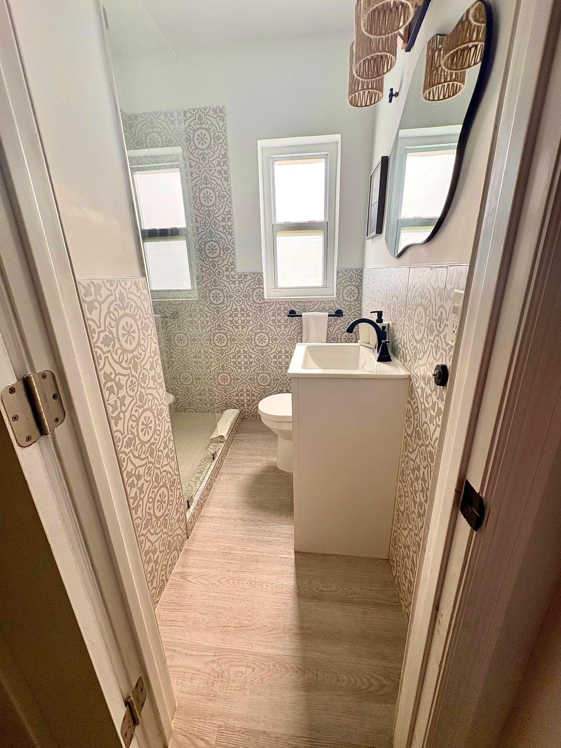 Narrow bathroom with patterned wallpaper, white vanity, and rug.