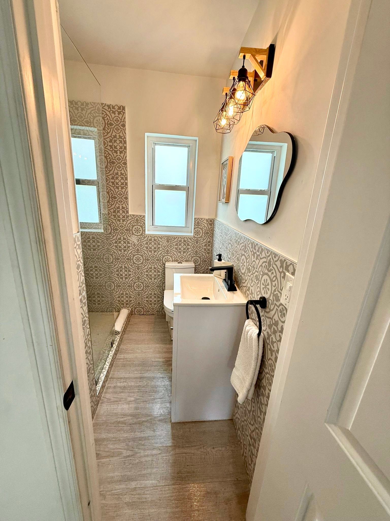 Narrow bathroom with patterned tile, a white vanity, and a small window.