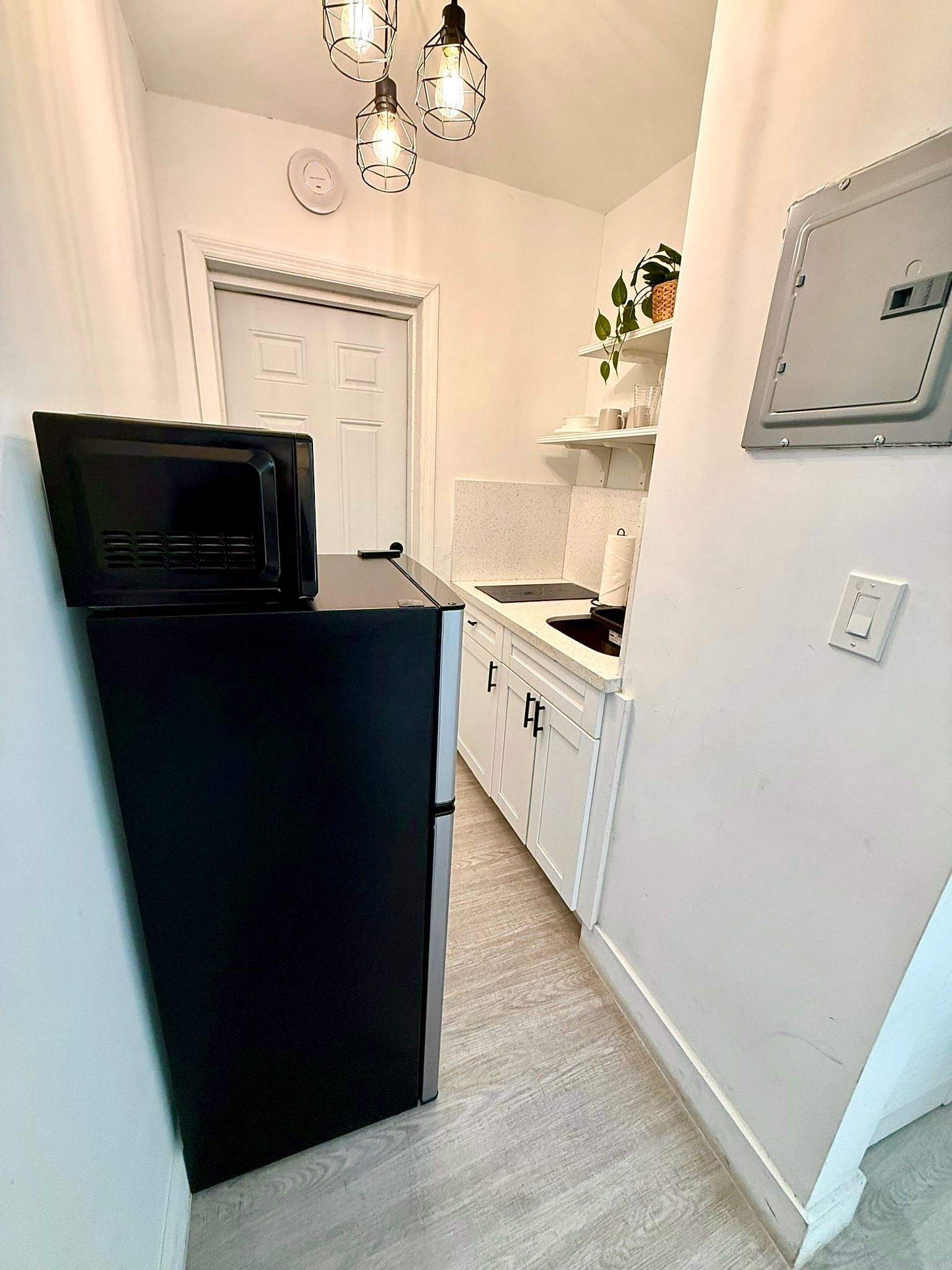 Narrow kitchen with black refrigerator, white cabinets, and open shelves.