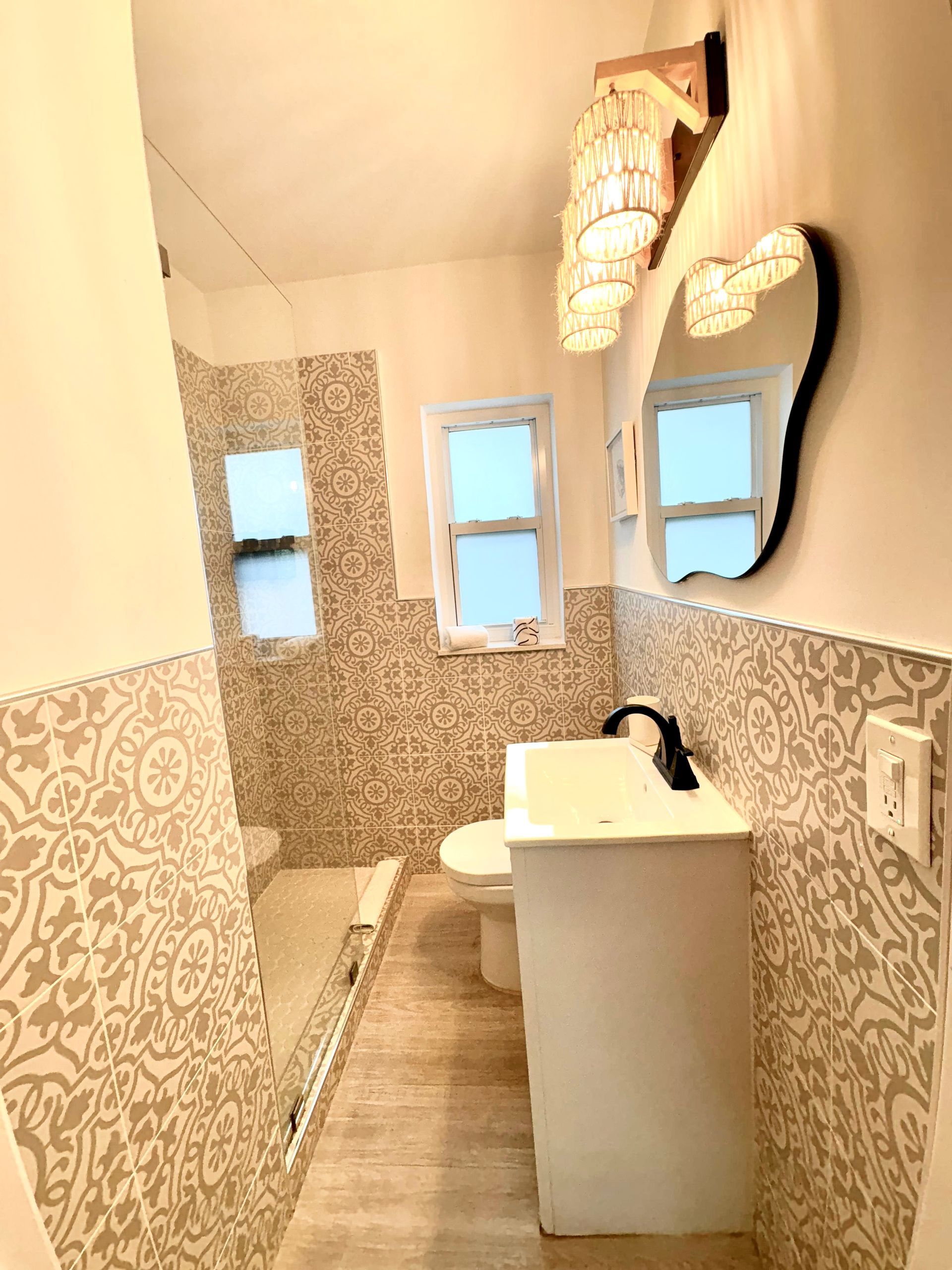 Bathroom with patterned tile walls, white vanity, and a unique-shaped mirror.