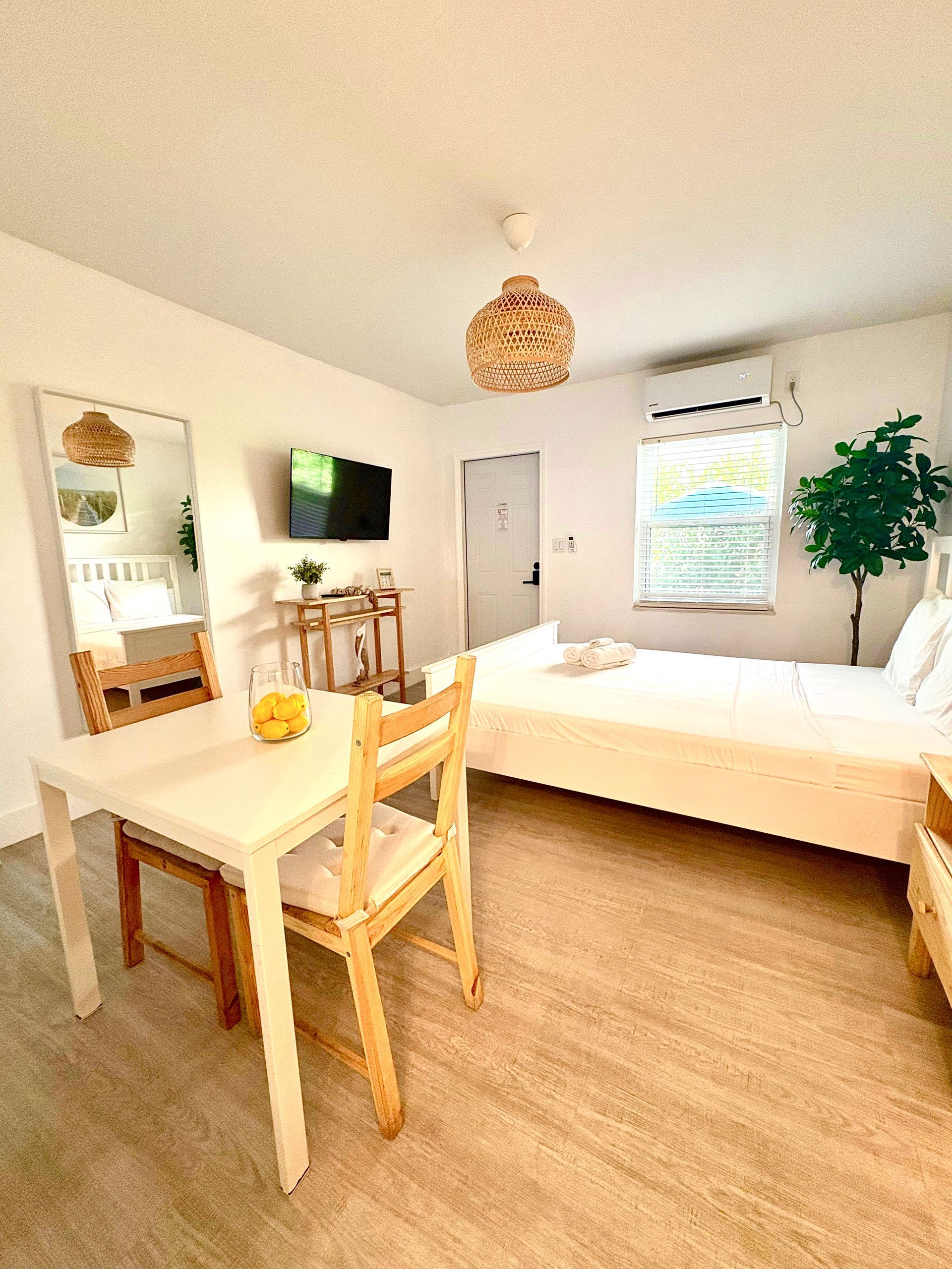 Small white studio apartment with bed, dining table, and a woven light fixture.
