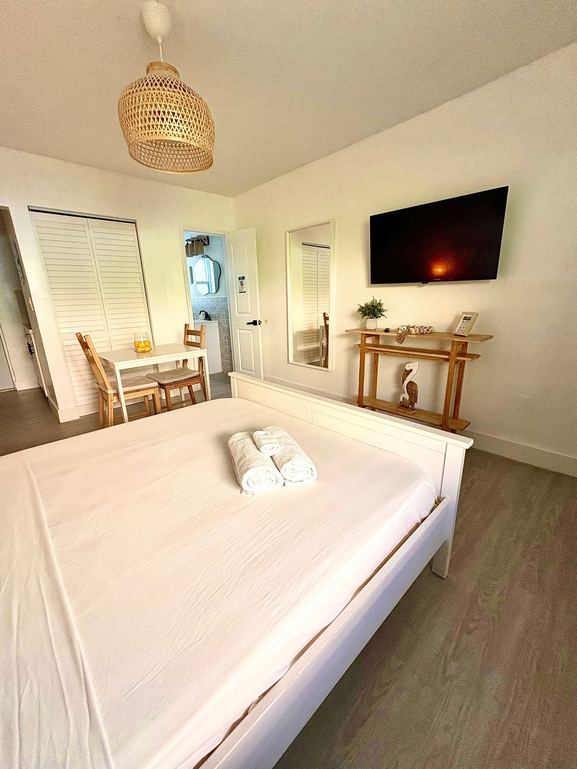 White bedroom with a bed, TV, and small dining area.