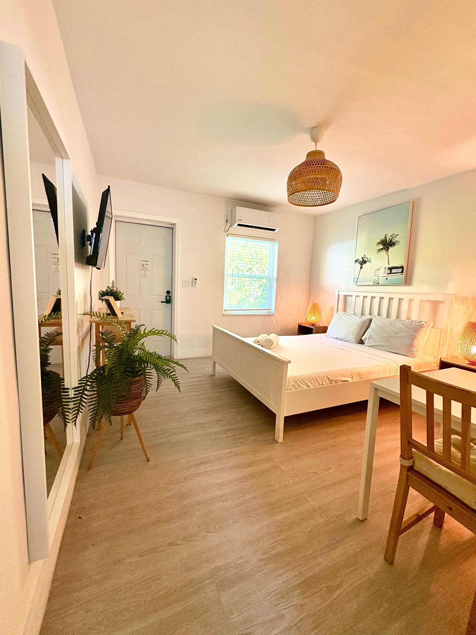 Bright bedroom with white bed, wall mirror, fern, artwork, and woven light fixture.