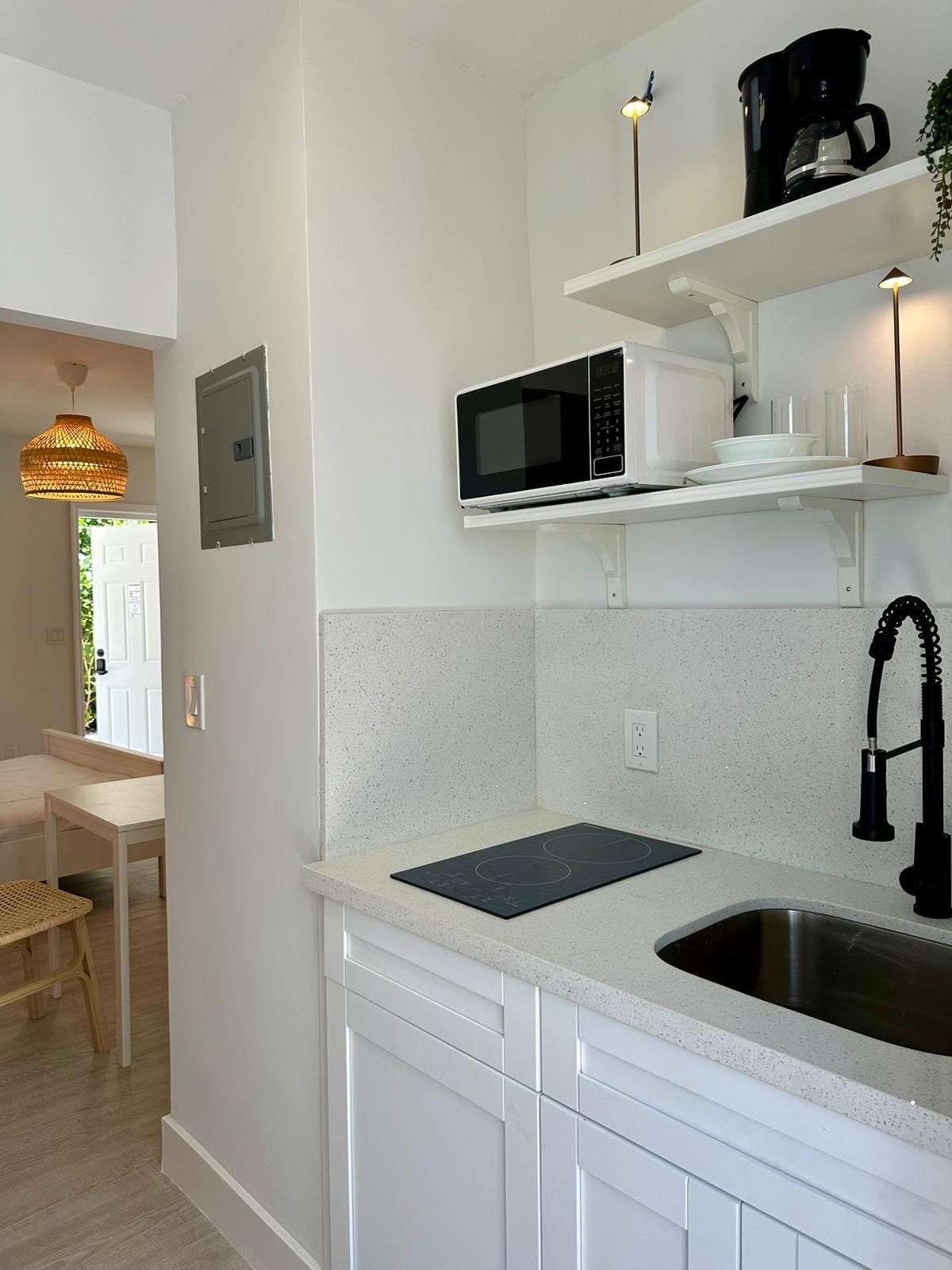 Small kitchen with white cabinets, microwave, coffee maker, and sink. Room leads to a bedroom.