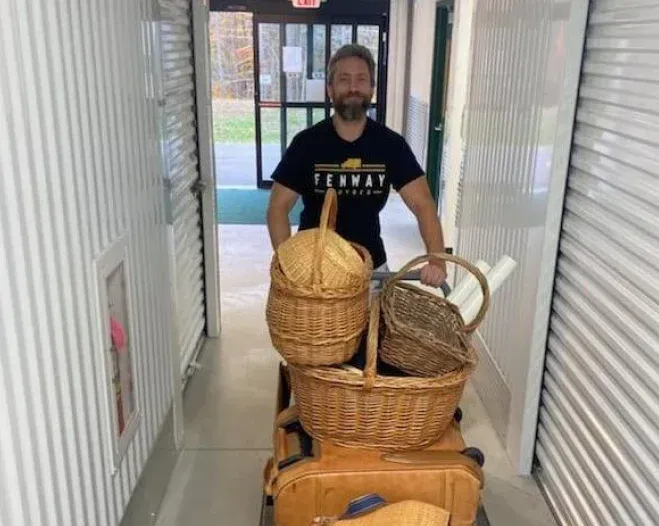 A man is pushing a cart filled with wicker baskets and suitcases.