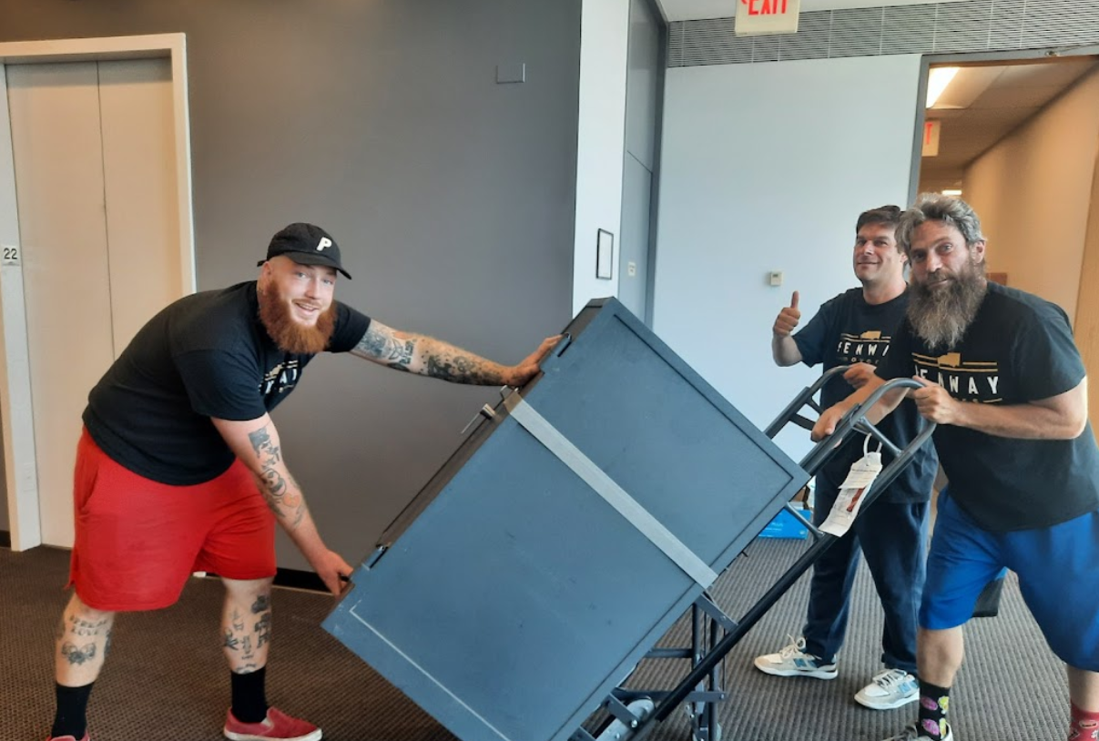 Three men are pushing a large black box on a cart.
