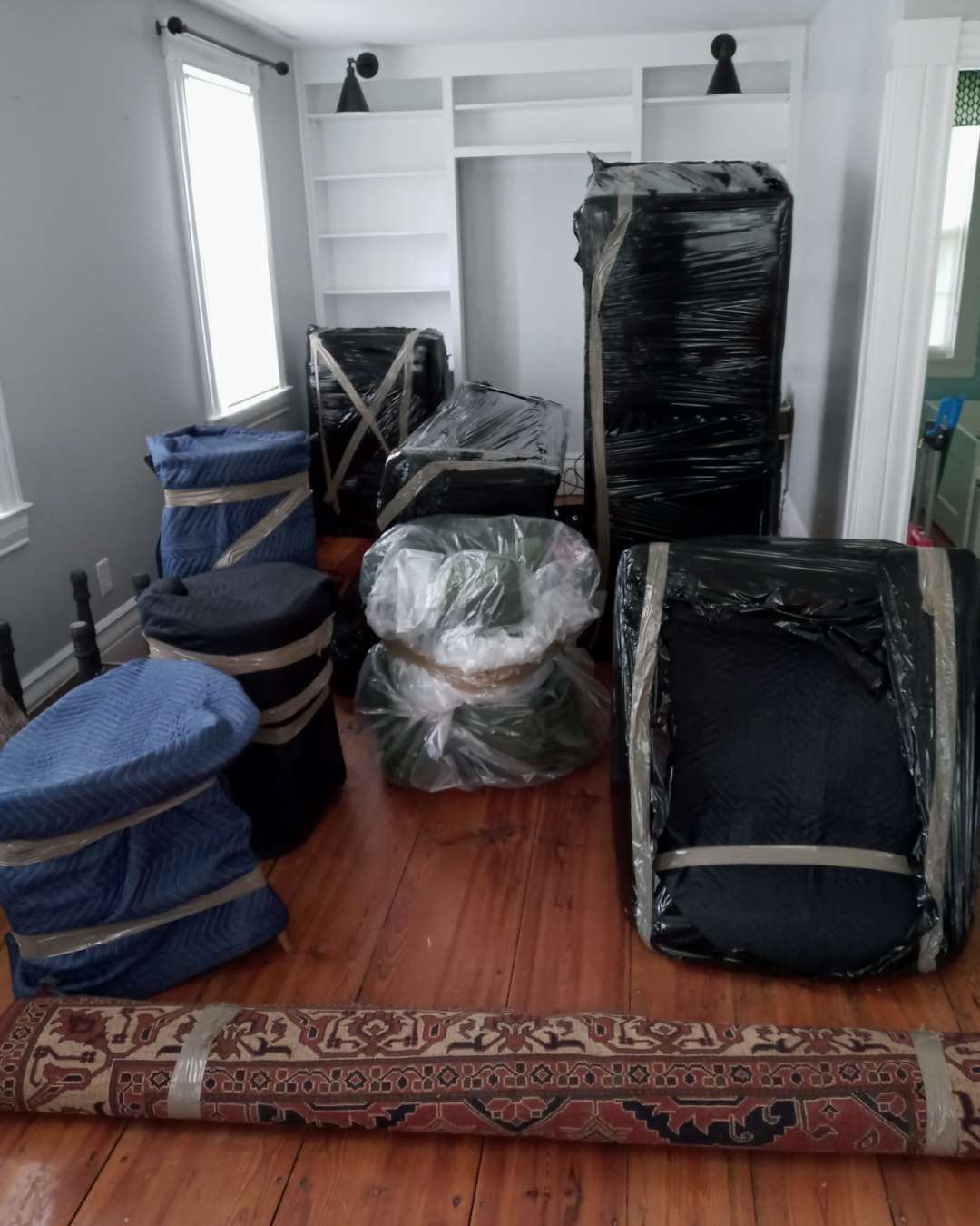 A living room filled with furniture wrapped in plastic and tape.