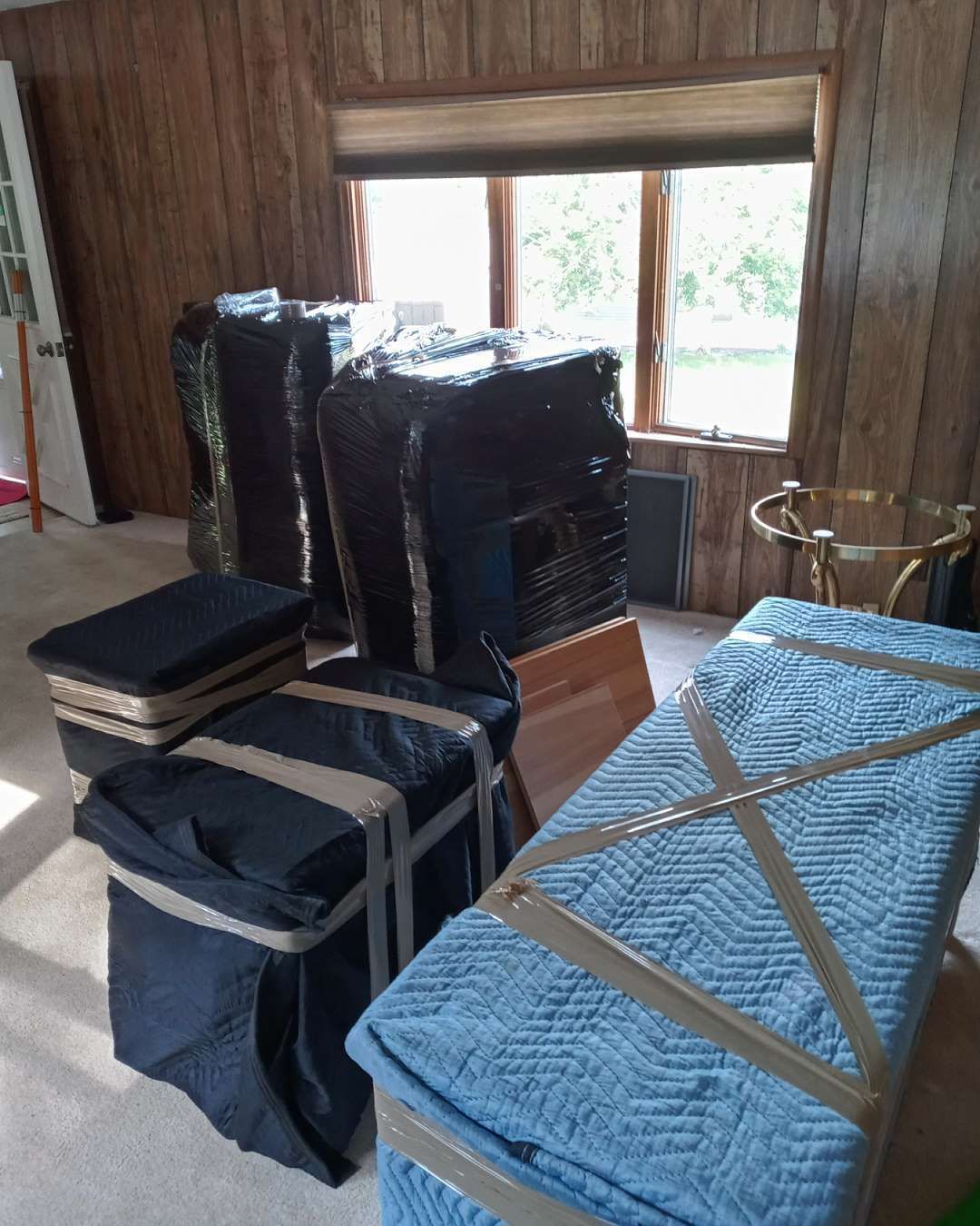 A living room filled with furniture wrapped in plastic and tape.