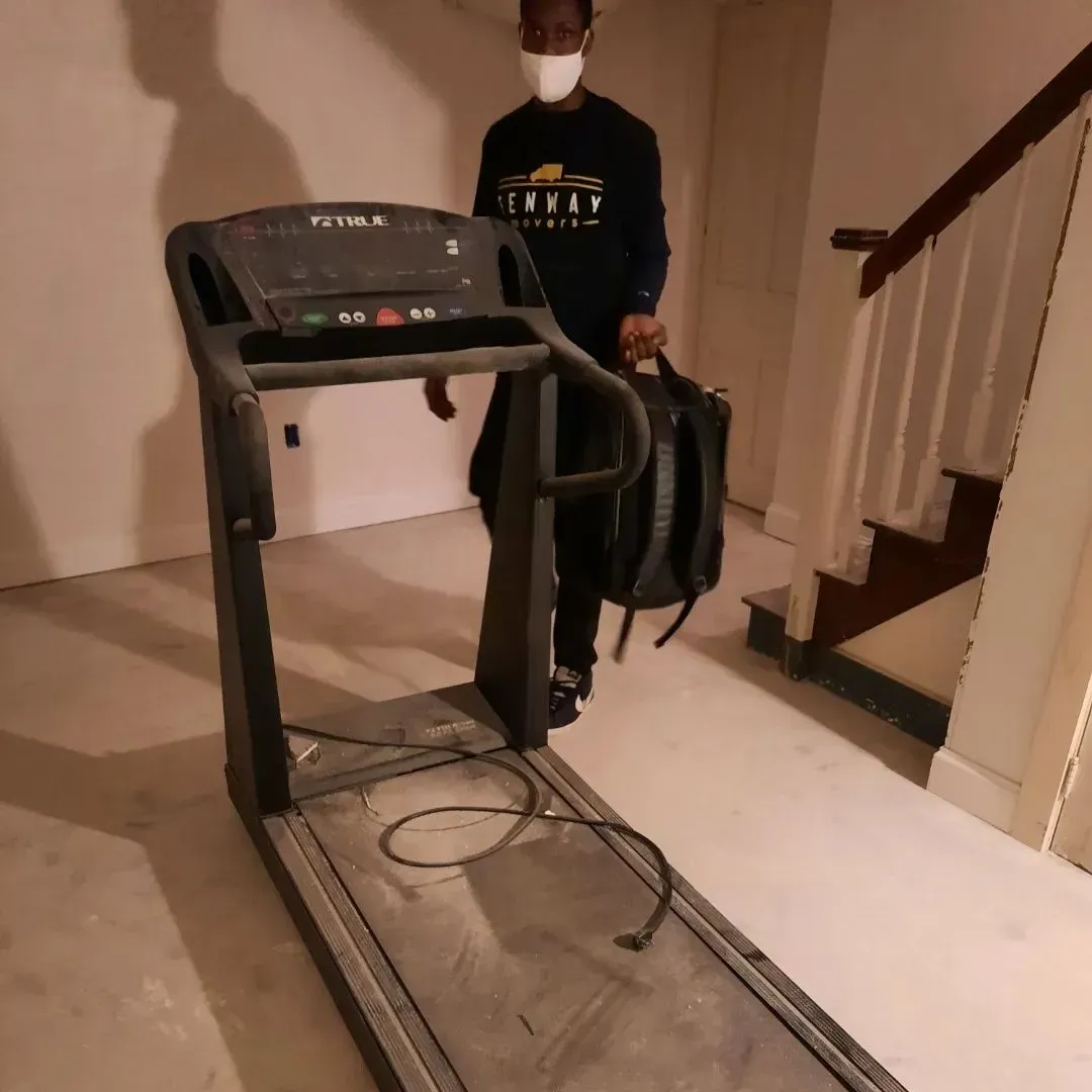 A man wearing a mask is standing next to a treadmill