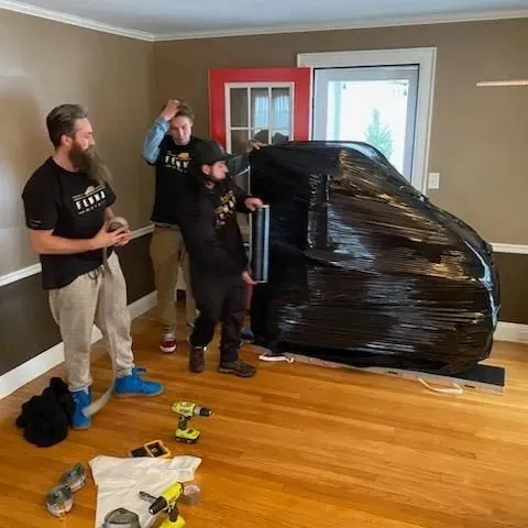 A group of men are moving a piano in a living room.