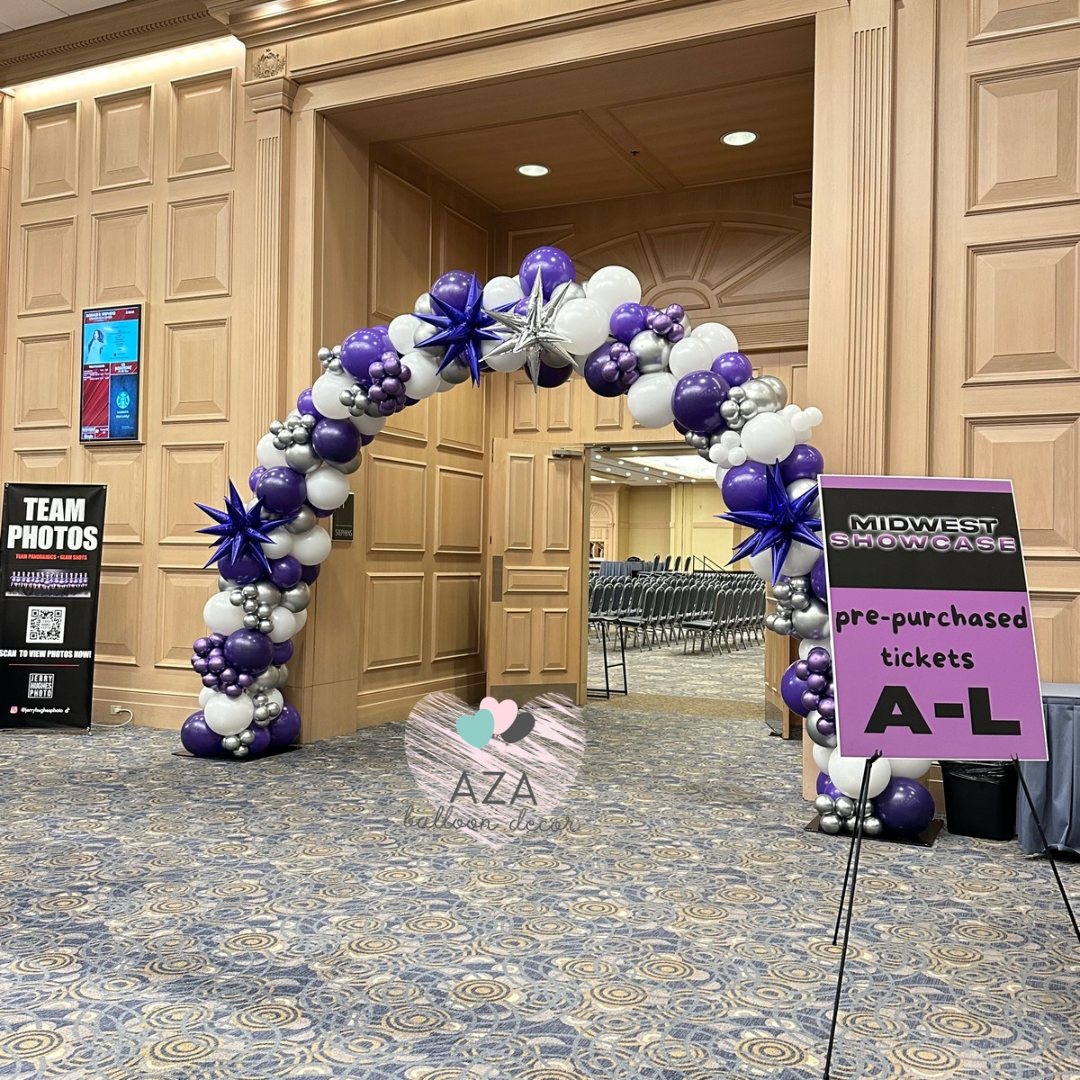 A purple , white and silver balloon arch in a hallway.