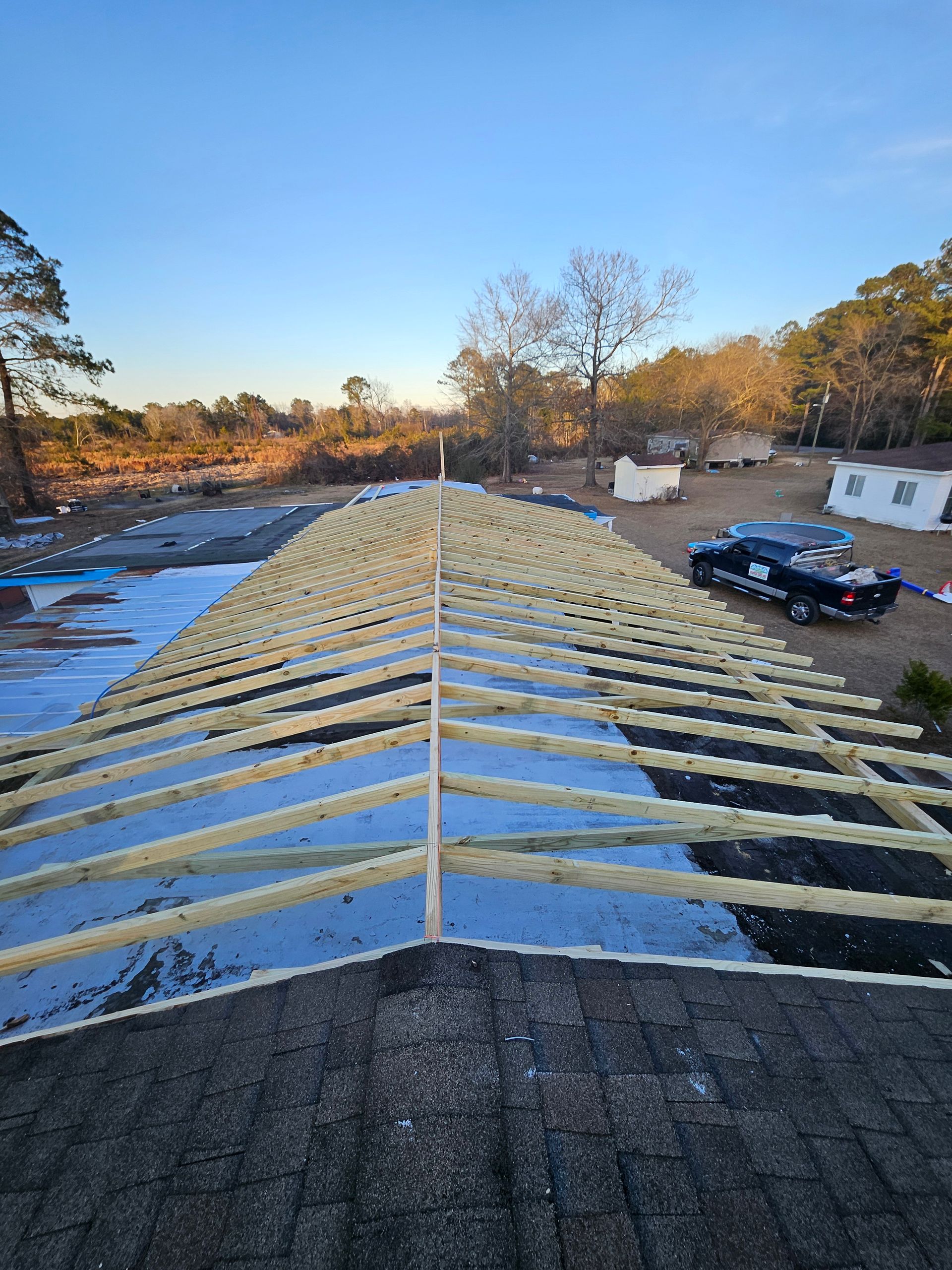 Roof under construction with wooden beams and a blue tarp covering. A pickup truck is parked nearby.