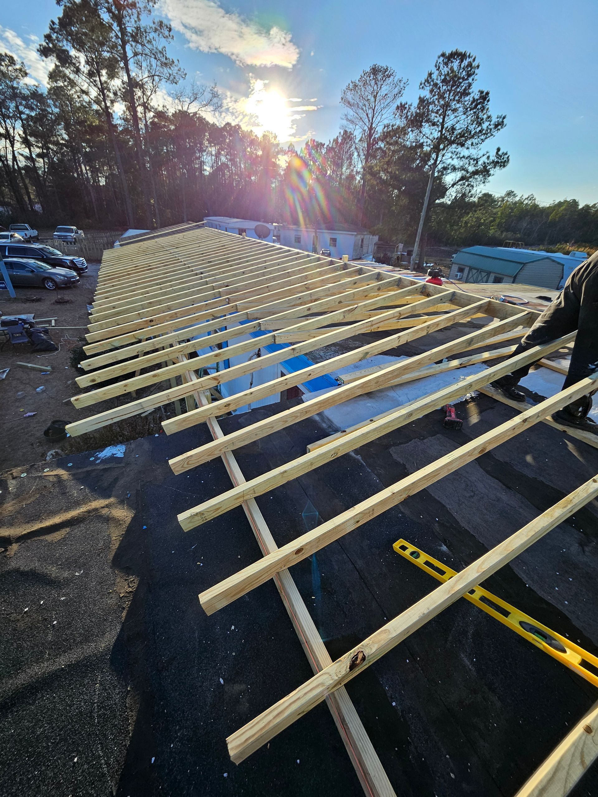 Construction of a roof framework on a building. Wooden beams laid on black roofing with a worker nearby. Sun shining.