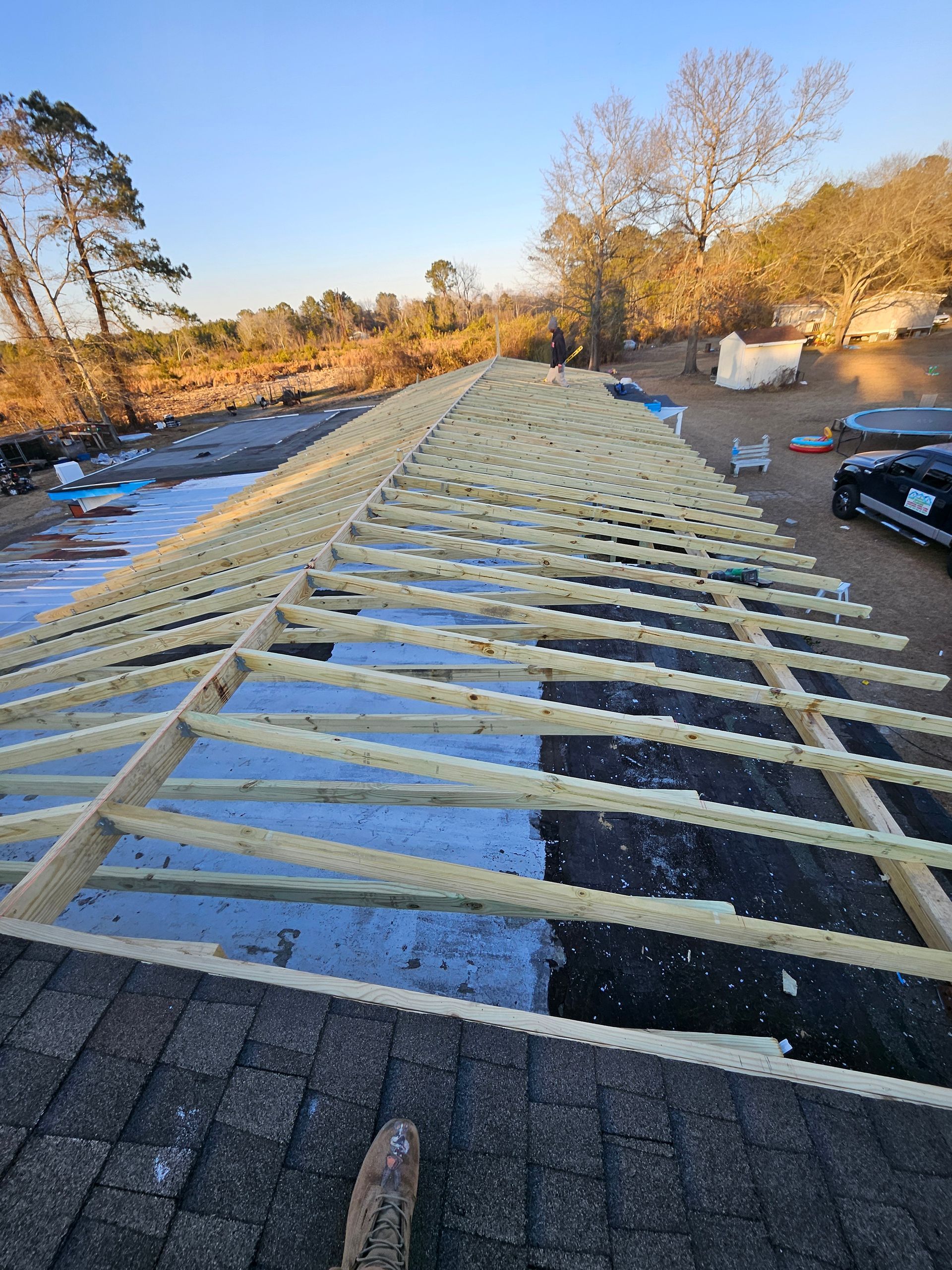 Roof construction in progress, wooden beams over shingles, sunny outdoor setting.