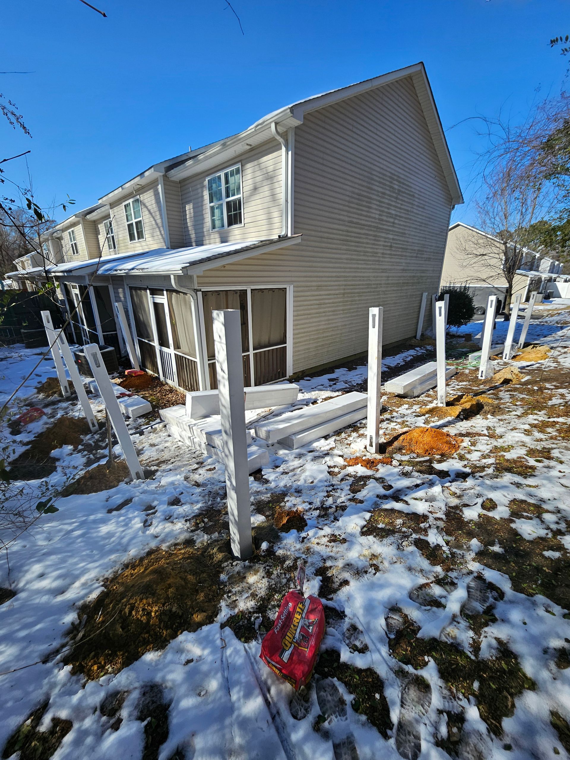 Snowy backyard with fence posts and house. Winter scene with bright blue sky.