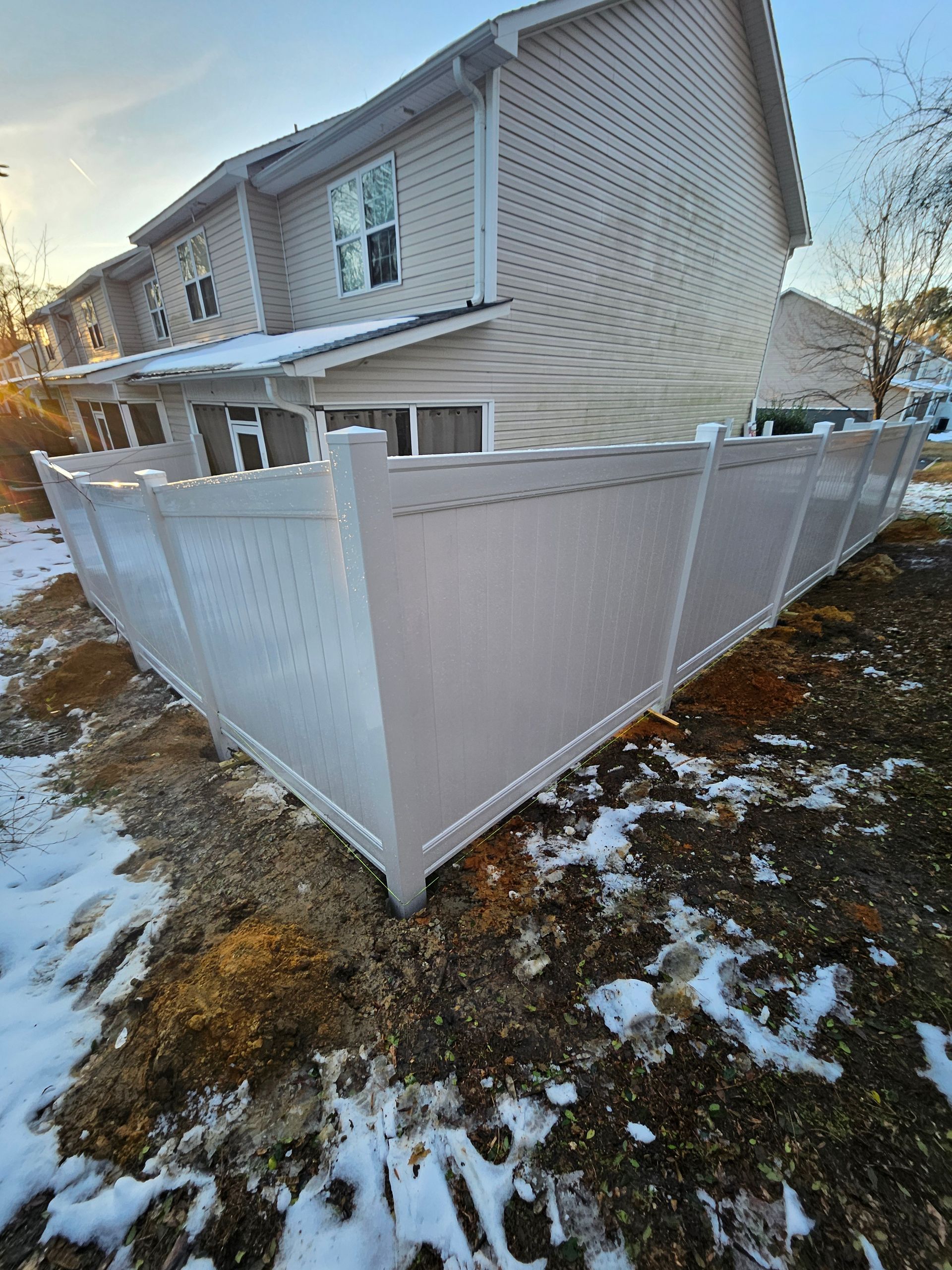 White vinyl fence in front of a tan two-story building on a snow-covered ground.