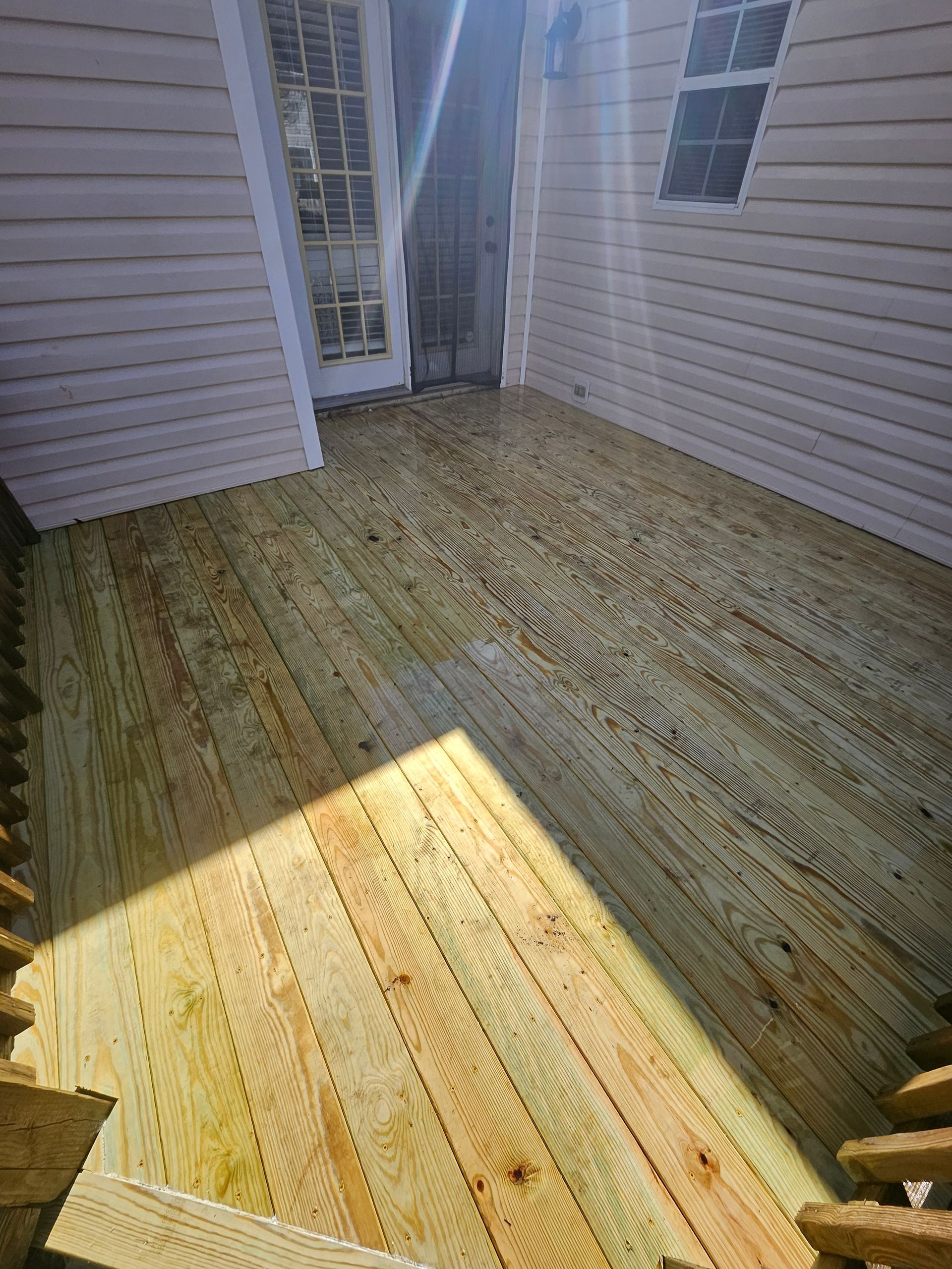 Wooden deck with white siding and door, sunlight creates shadows.