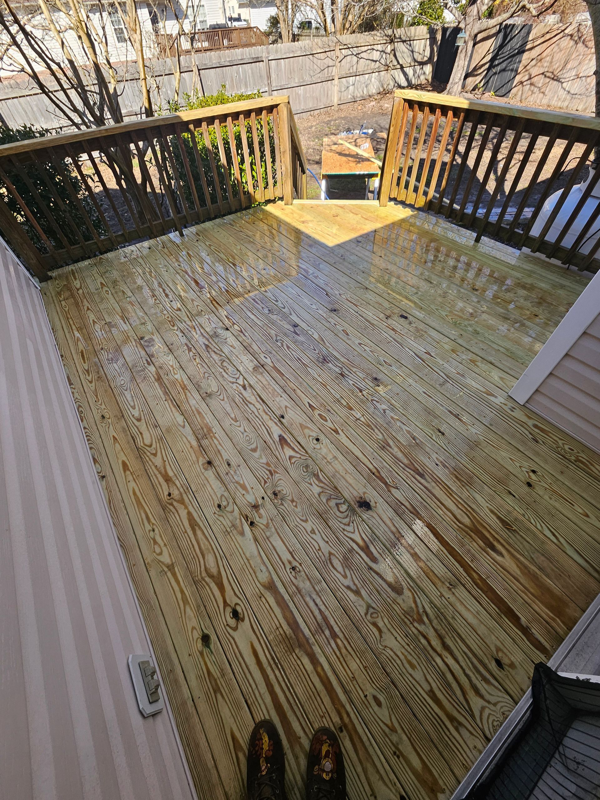 Wooden deck with railings, viewed from above, boots in foreground.
