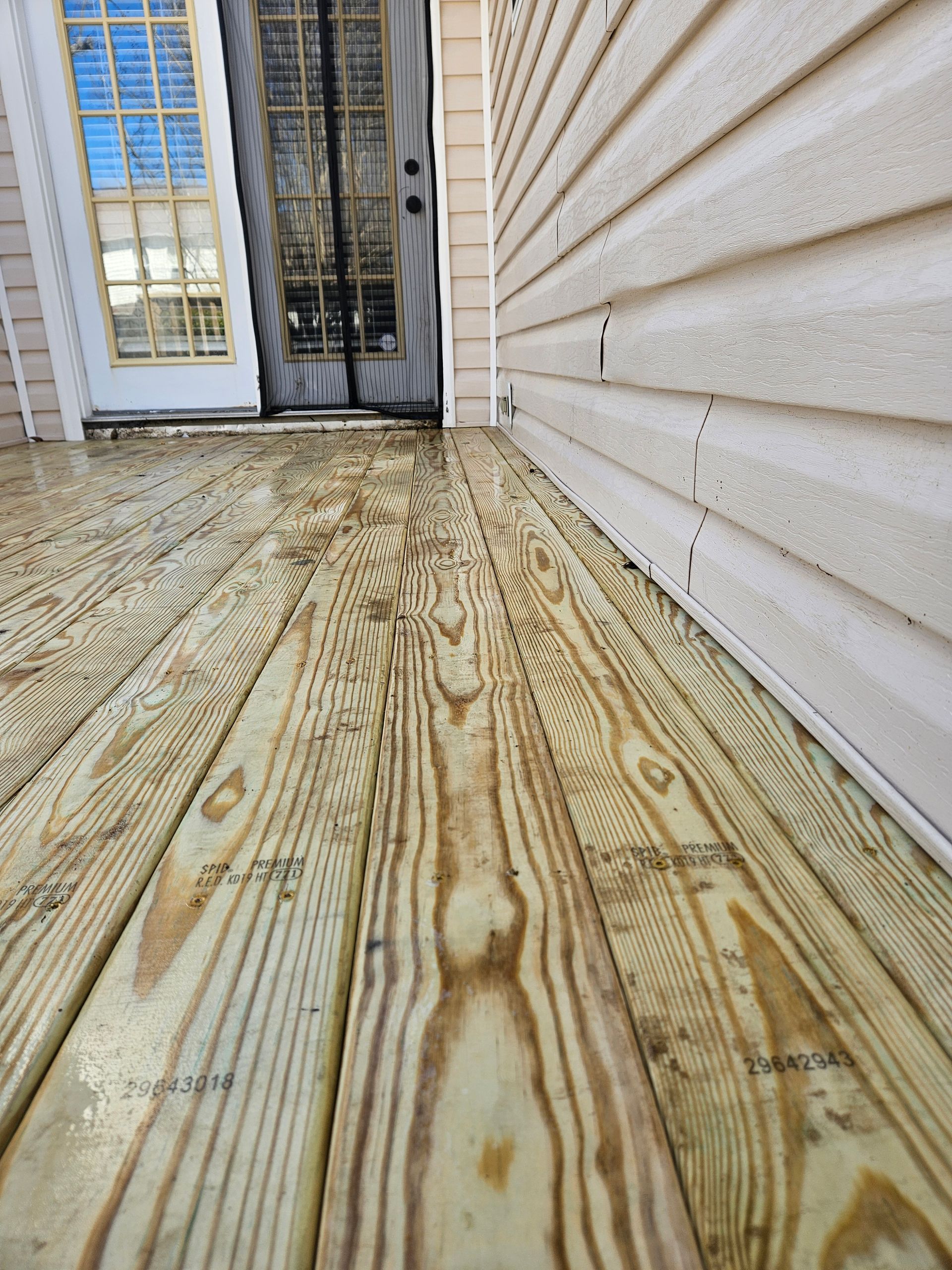 Wooden deck leading to a screen door and a siding wall. Light wood planks, angled shot.